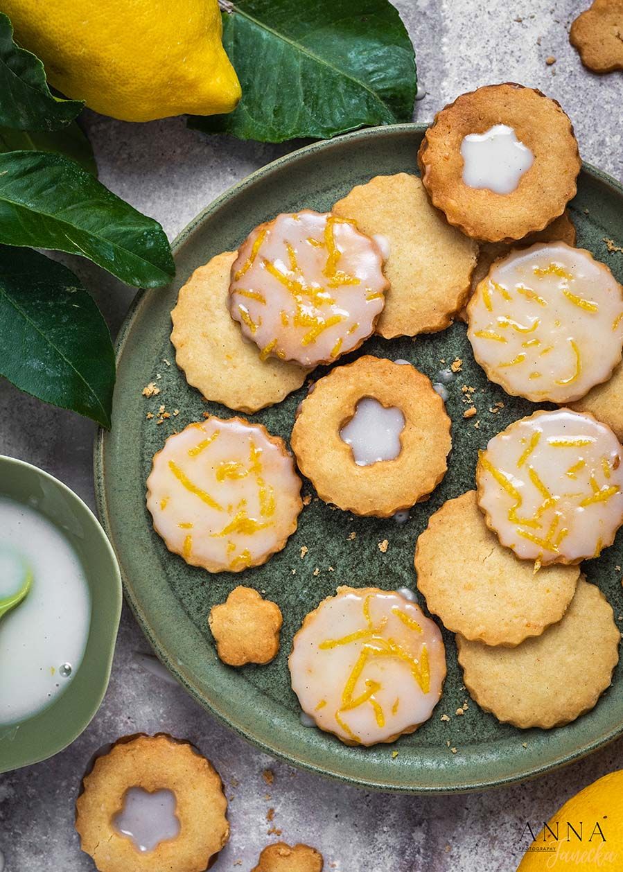 Lemon shortbread cookies with white icing and yellow zest on a green plate.