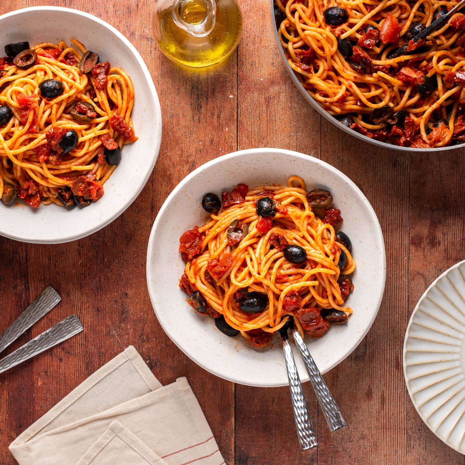 Two bowls of pasta with red sauce and olives served on a rustic wooden table.