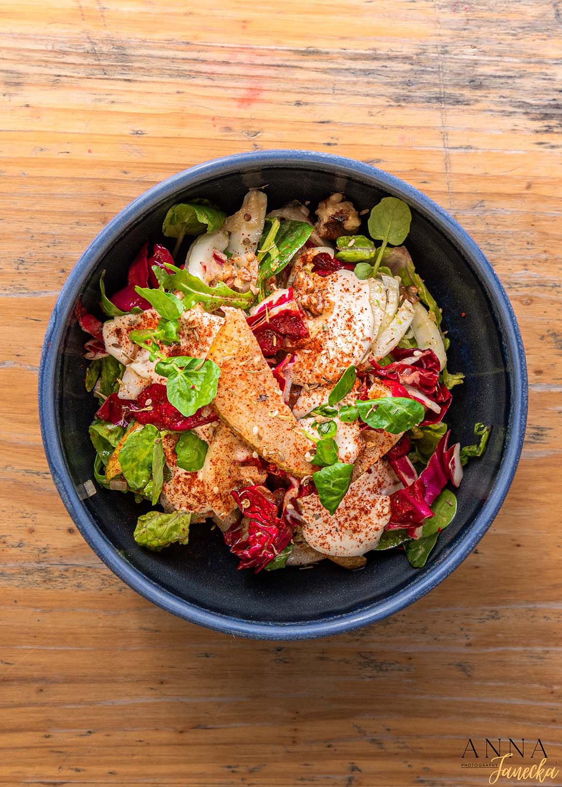 Fresh salad bowl with grilled chicken, mixed greens, and colorful vegetables on wooden surface.