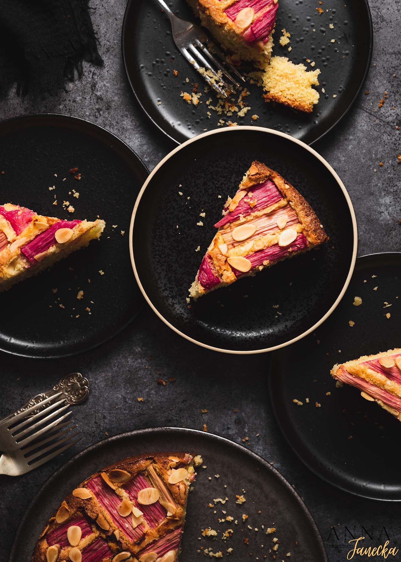 Slices of pink-topped almond cake served on black plates with golden rim.