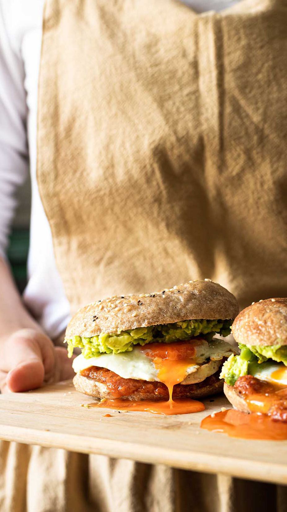 Juicy cheeseburgers with lettuce and melted cheese served on a wooden cutting board next to a brown paper bag.