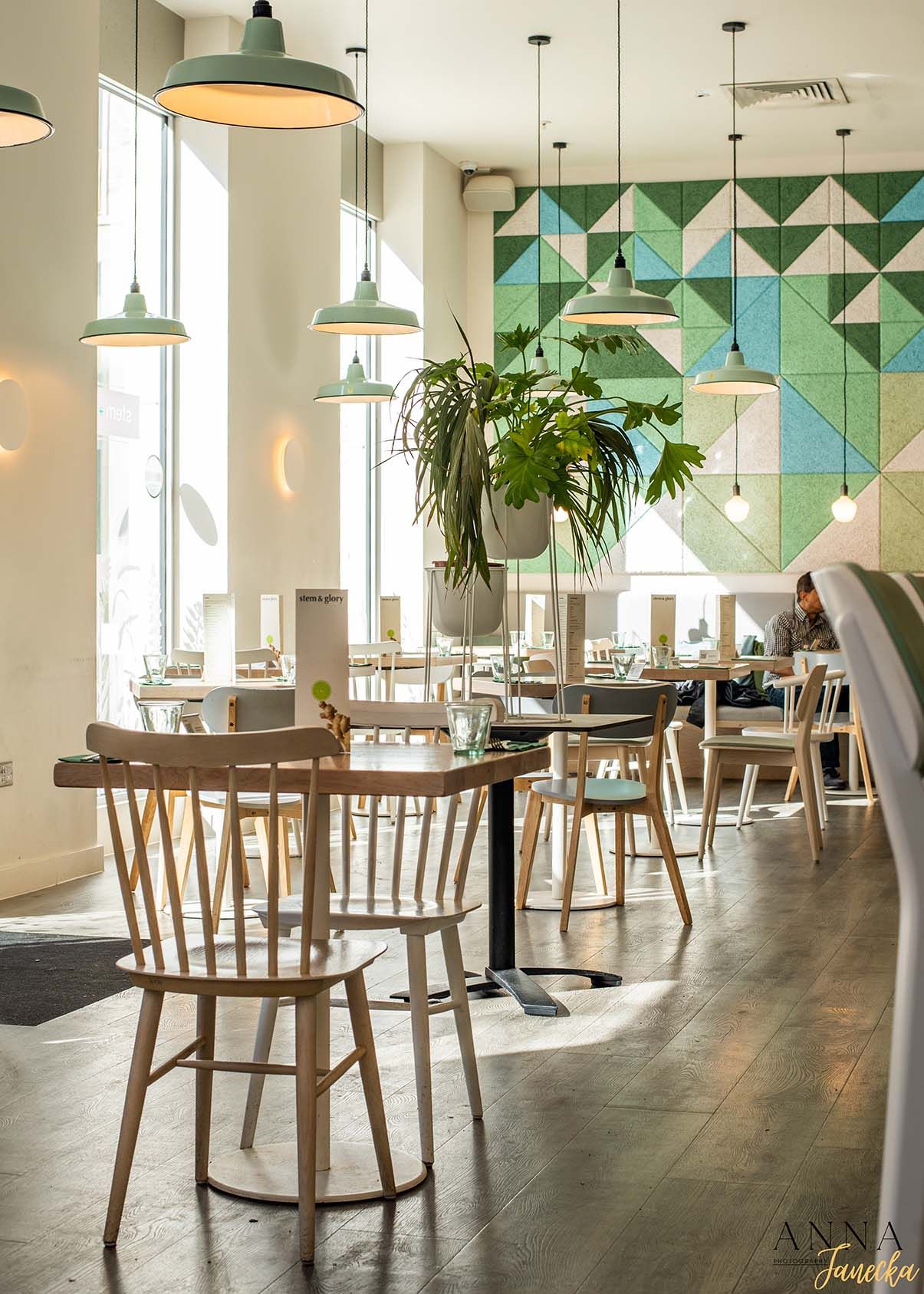 Modern restaurant interior with geometric teal wall tiles and wooden chairs under pendant lighting.
