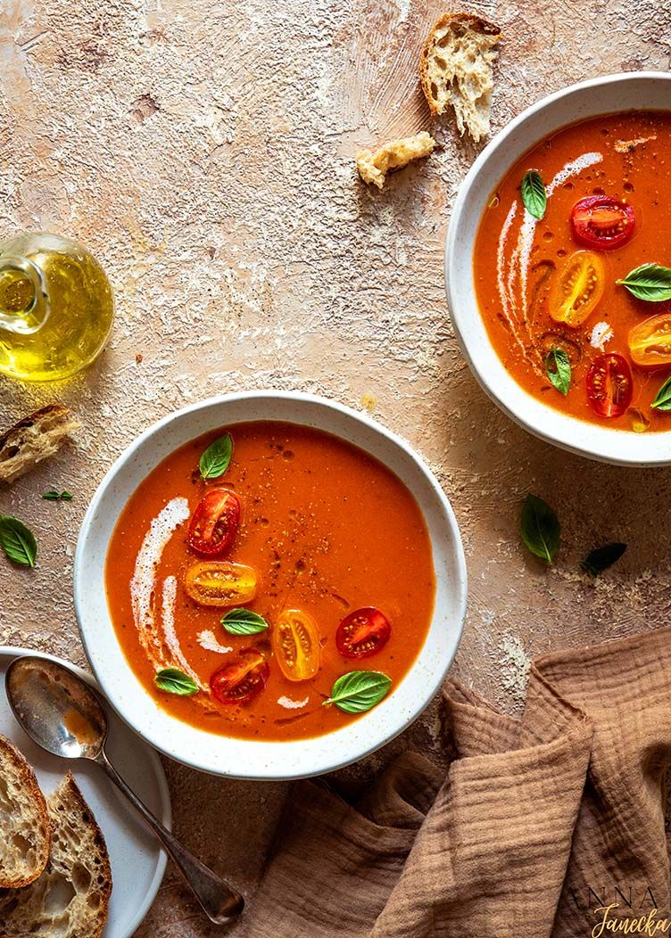 Creamy tomato soup garnished with cherry tomatoes, basil, and olive oil in white bowls.
