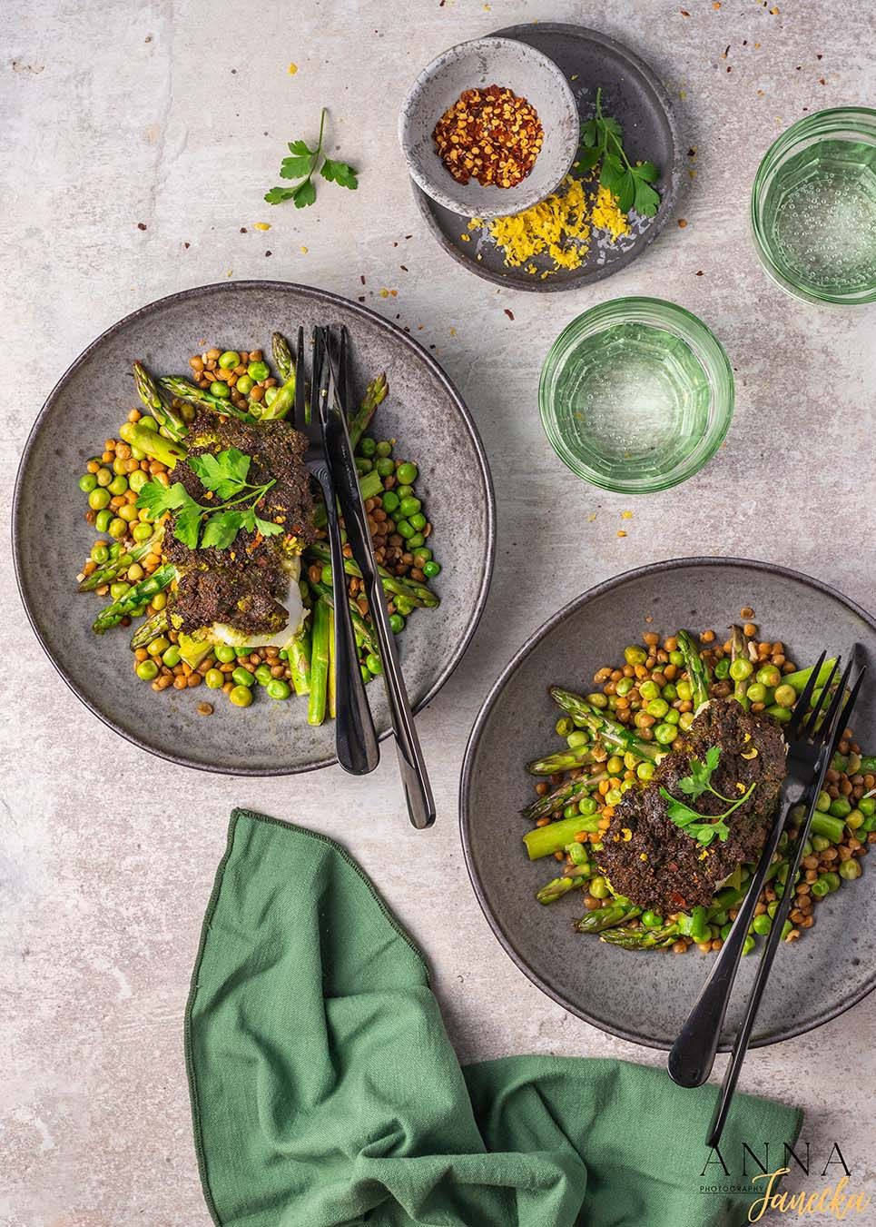 Grilled asparagus and green pea side dish served on dark ceramic plates with garnish.