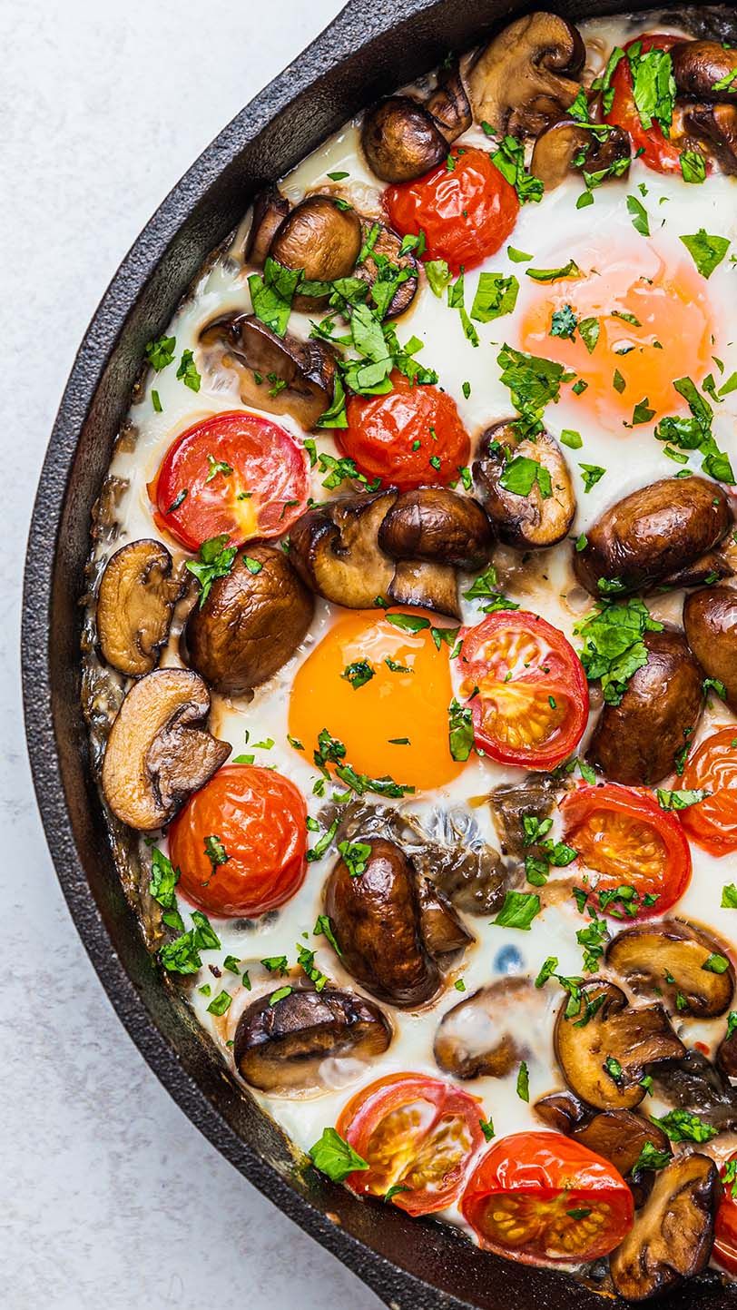 Sauteed mushrooms, roasted tomatoes and sunny side up eggs in a cast iron skillet garnished with fresh herbs.