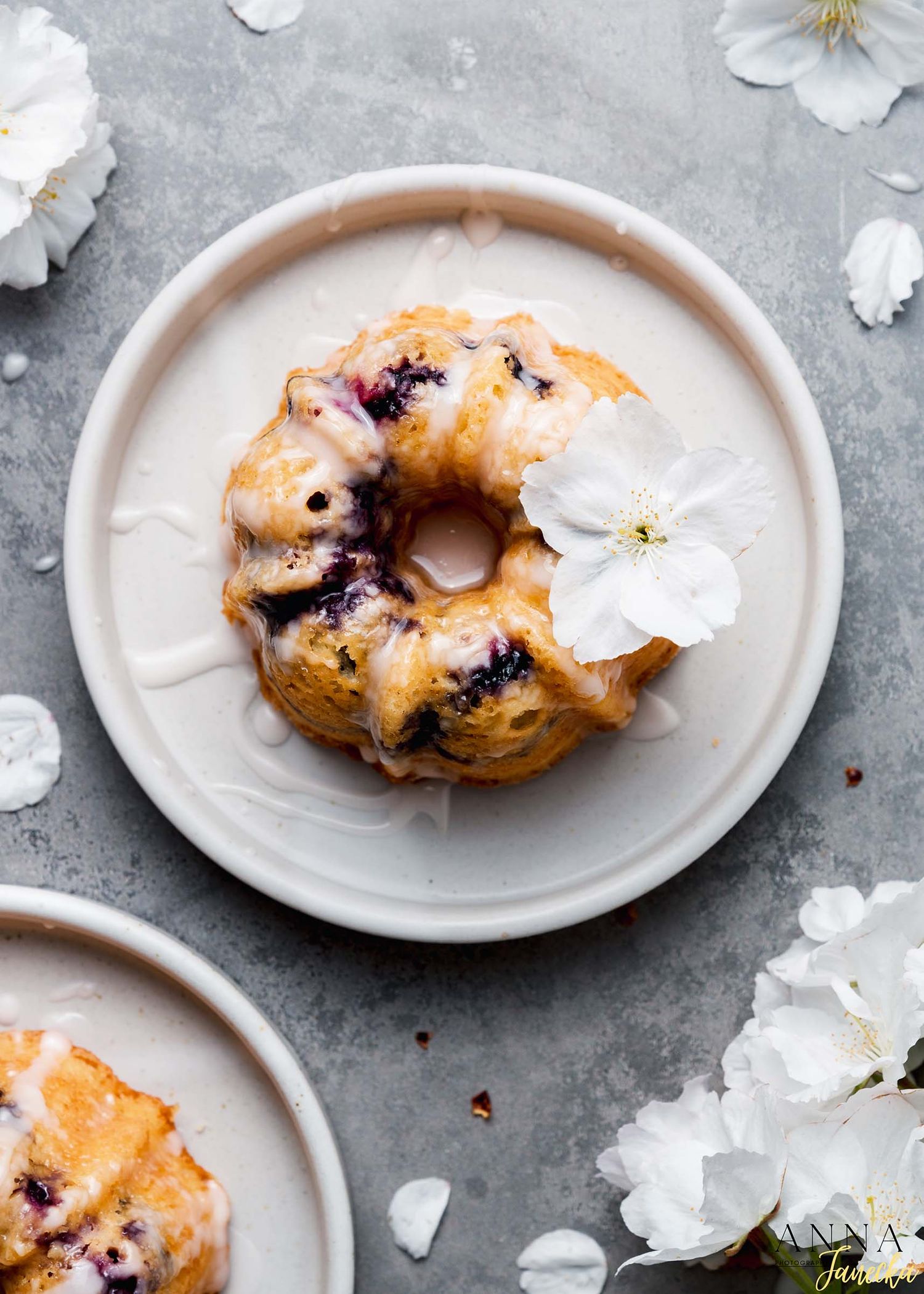 Glazed blueberry pastry garnished with white flowers on a light gray plate.