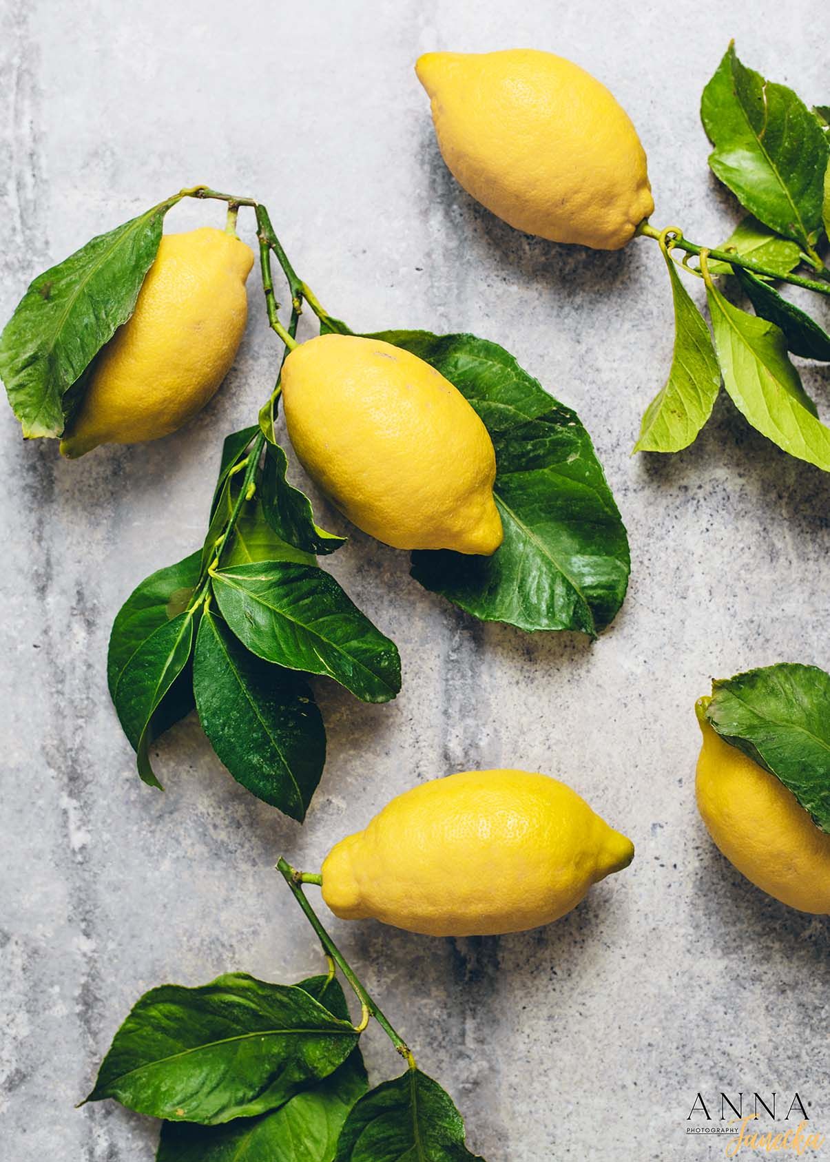Fresh yellow lemons with bright green leaves arranged on a light gray surface.