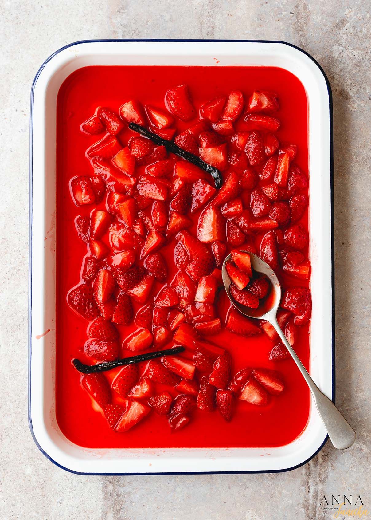 Red berry compote with vanilla pods in a white enamel baking dish.