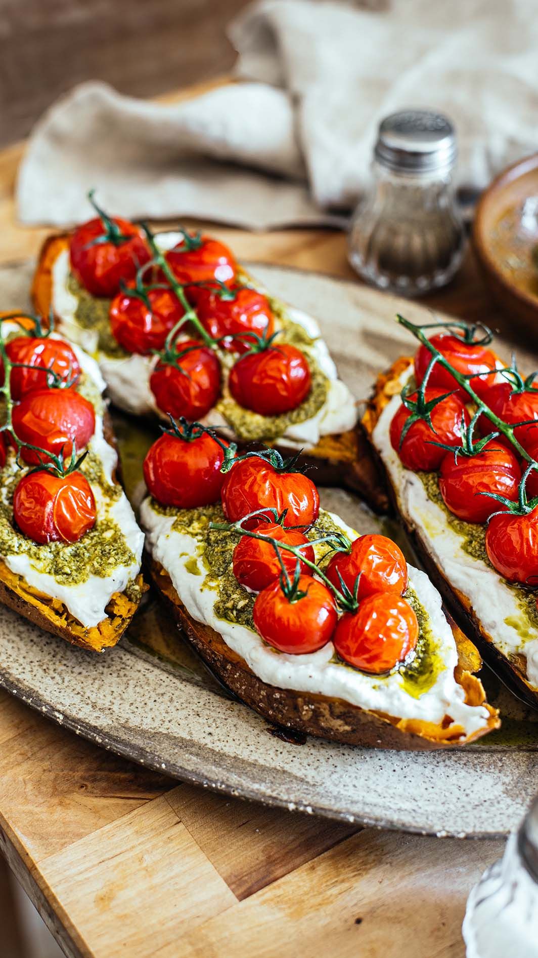 Rustic toast topped with ricotta cheese, pesto, and roasted cherry tomatoes on the vine served on a ceramic plate.