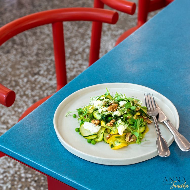 Fresh spring salad with greens and cheese served on white plate against blue table.