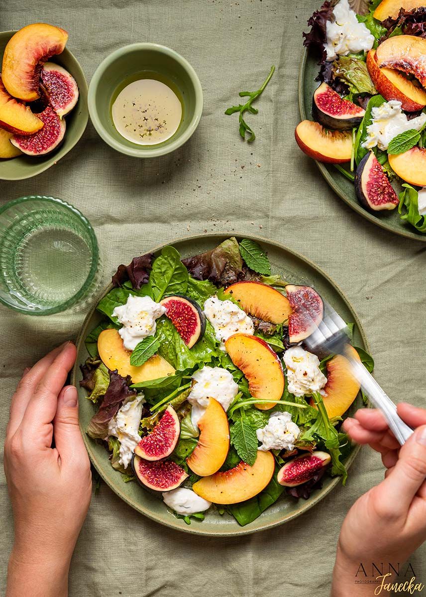 Fresh summer salad with peaches, figs, burrata cheese and mixed greens on a ceramic plate.