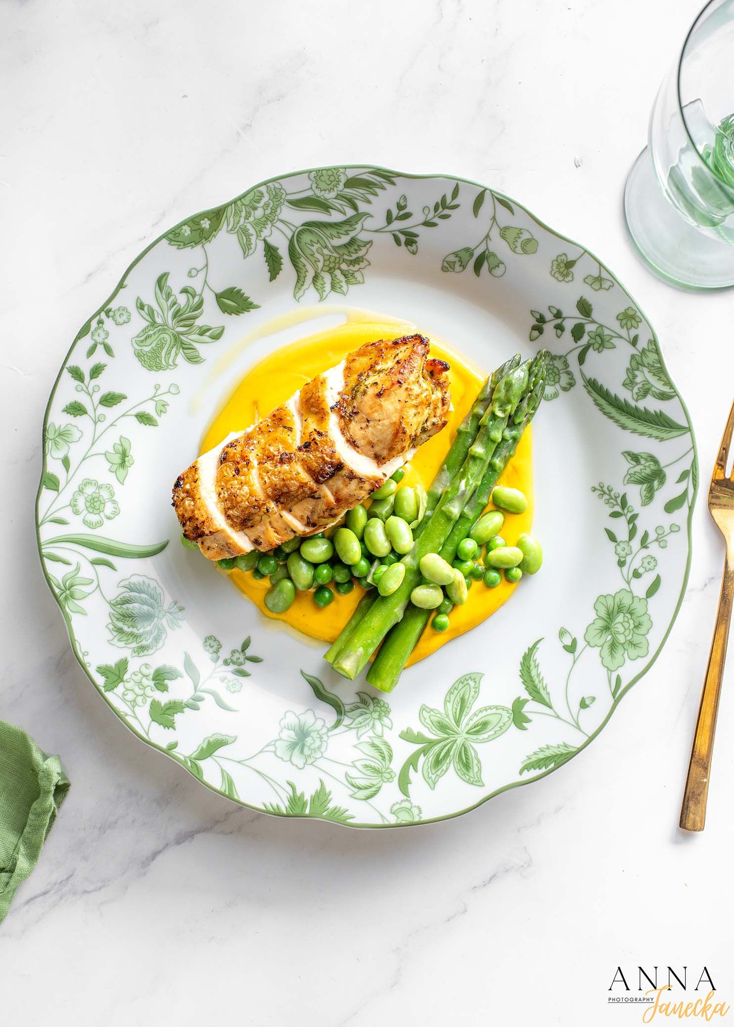 Pan-seared fish with asparagus and yellow sauce served on a decorative floral plate.