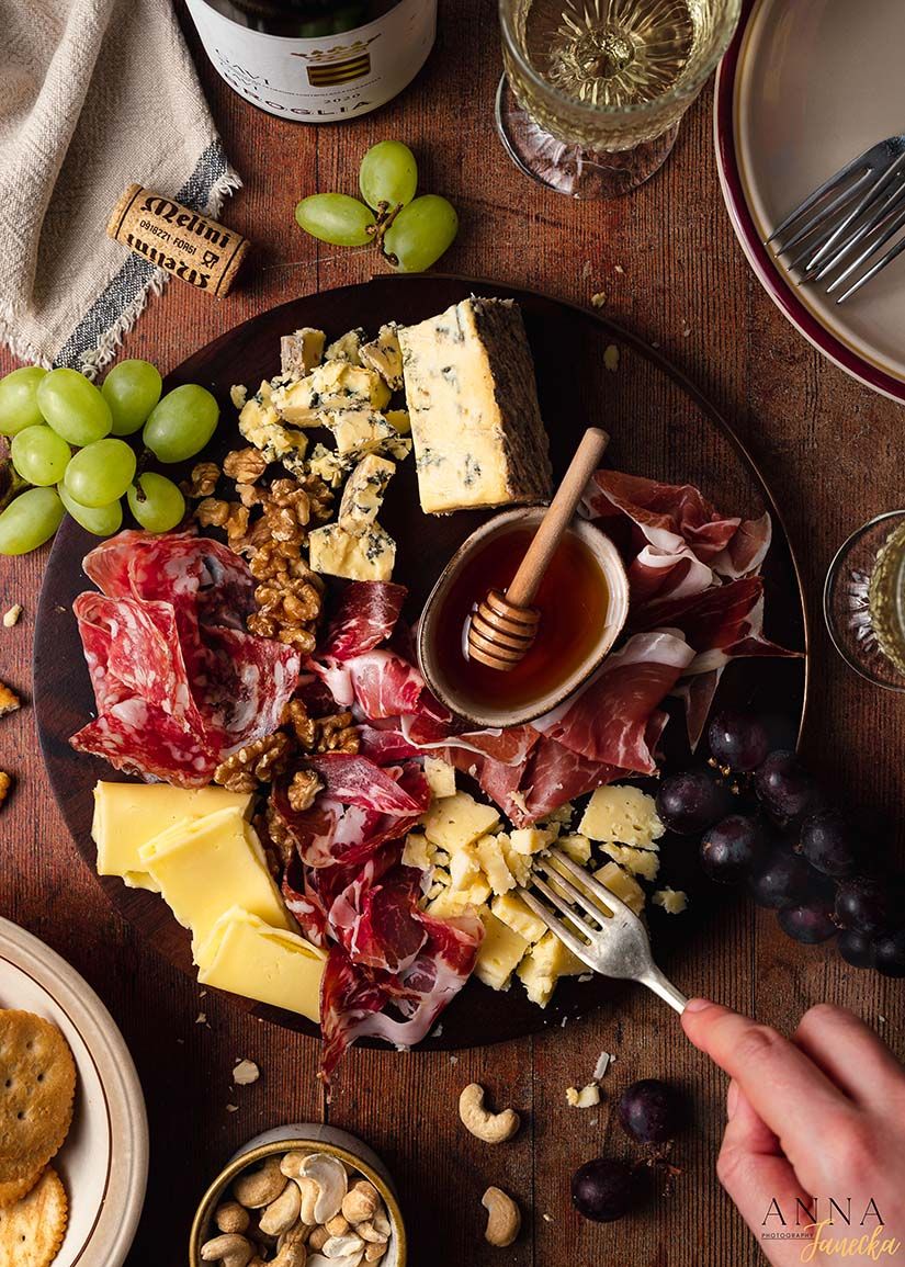 Gourmet cheese and charcuterie board with grapes, honey, and nuts on rustic wooden surface.