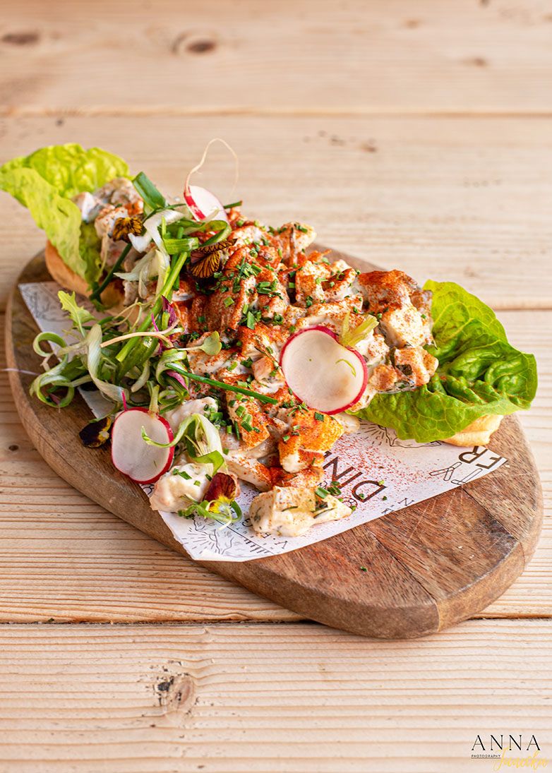 Grilled shrimp sandwich garnished with radishes and microgreens on wooden board.