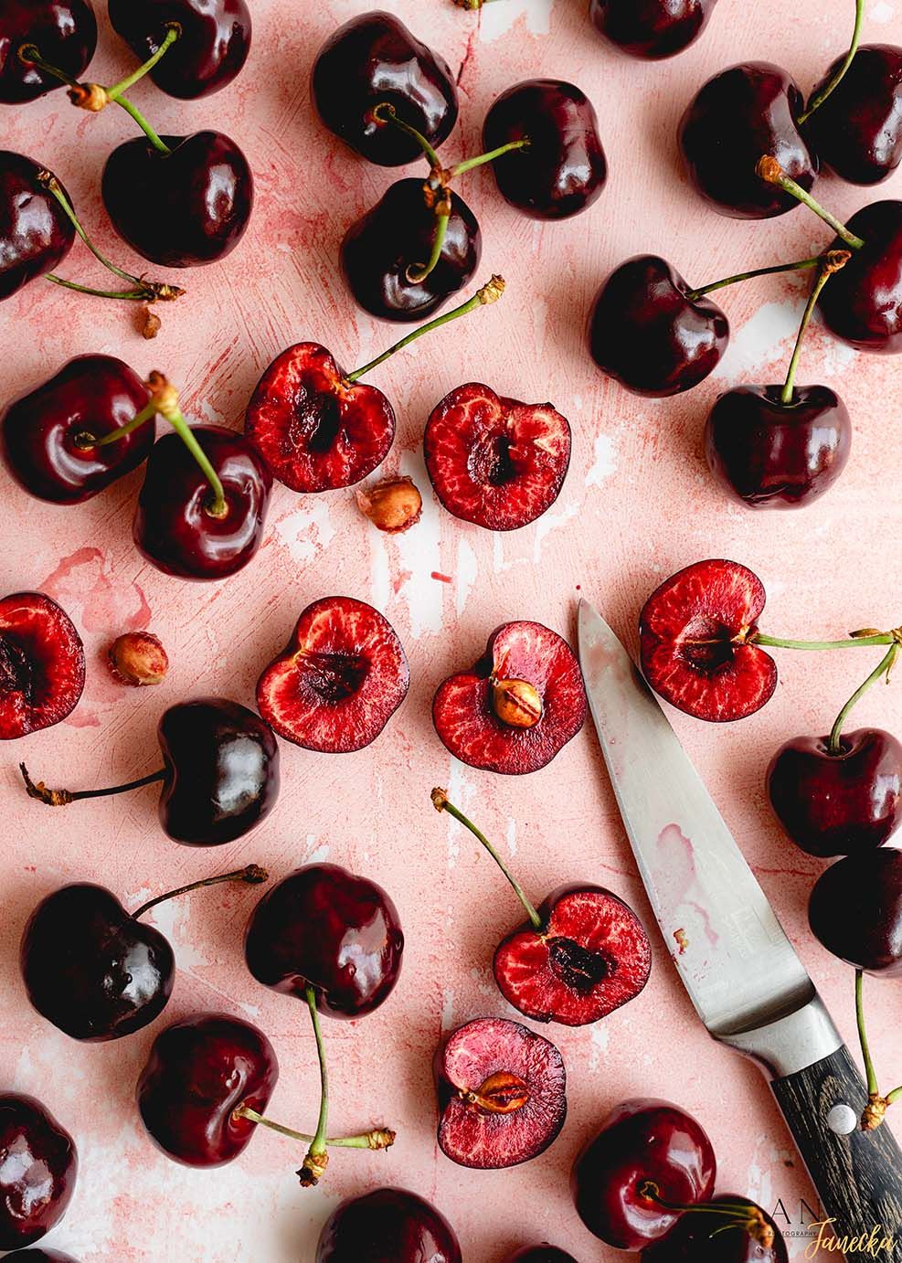 Fresh red cherries arranged on pink background with pits and stems visible.