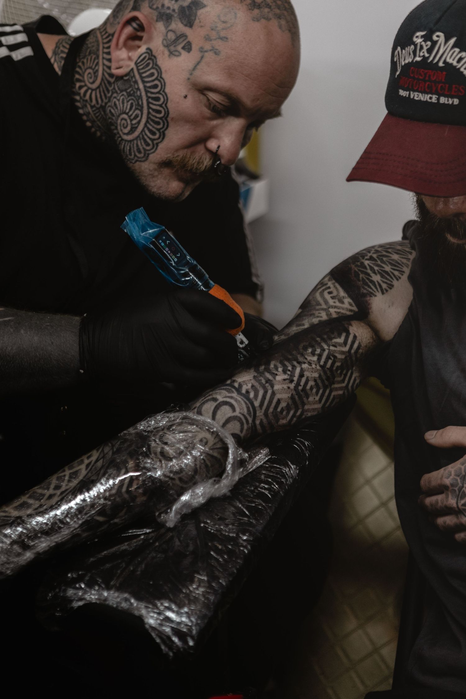 A tattooed artist wearing black applies plastic wrap to freshly completed tattoo work.