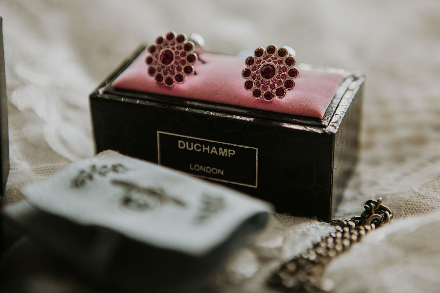 A pair of ornate copper flower stud earrings displayed on a pink box labeled Onchamp with jewelry in background.