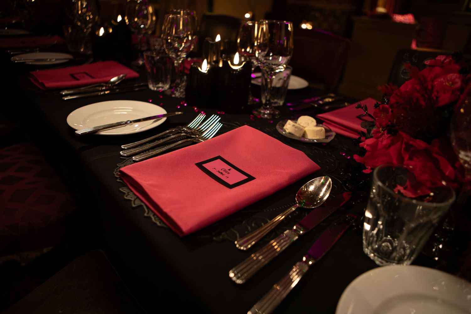Elegant table setting with red napkins, silverware, and wine glasses in a dark romantic restaurant atmosphere.