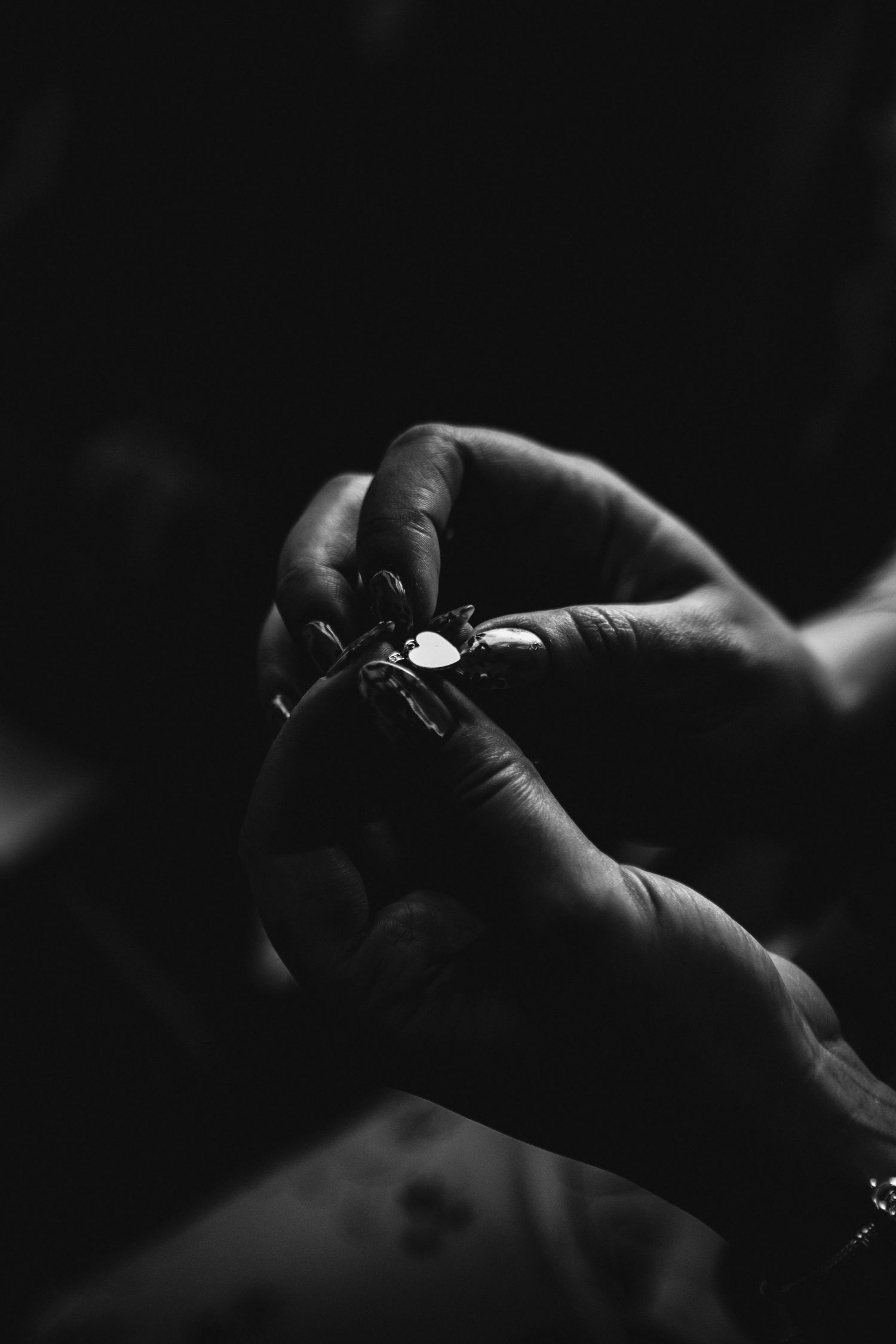 Black and white close-up photo of hands working with a small delicate object against a dark background.