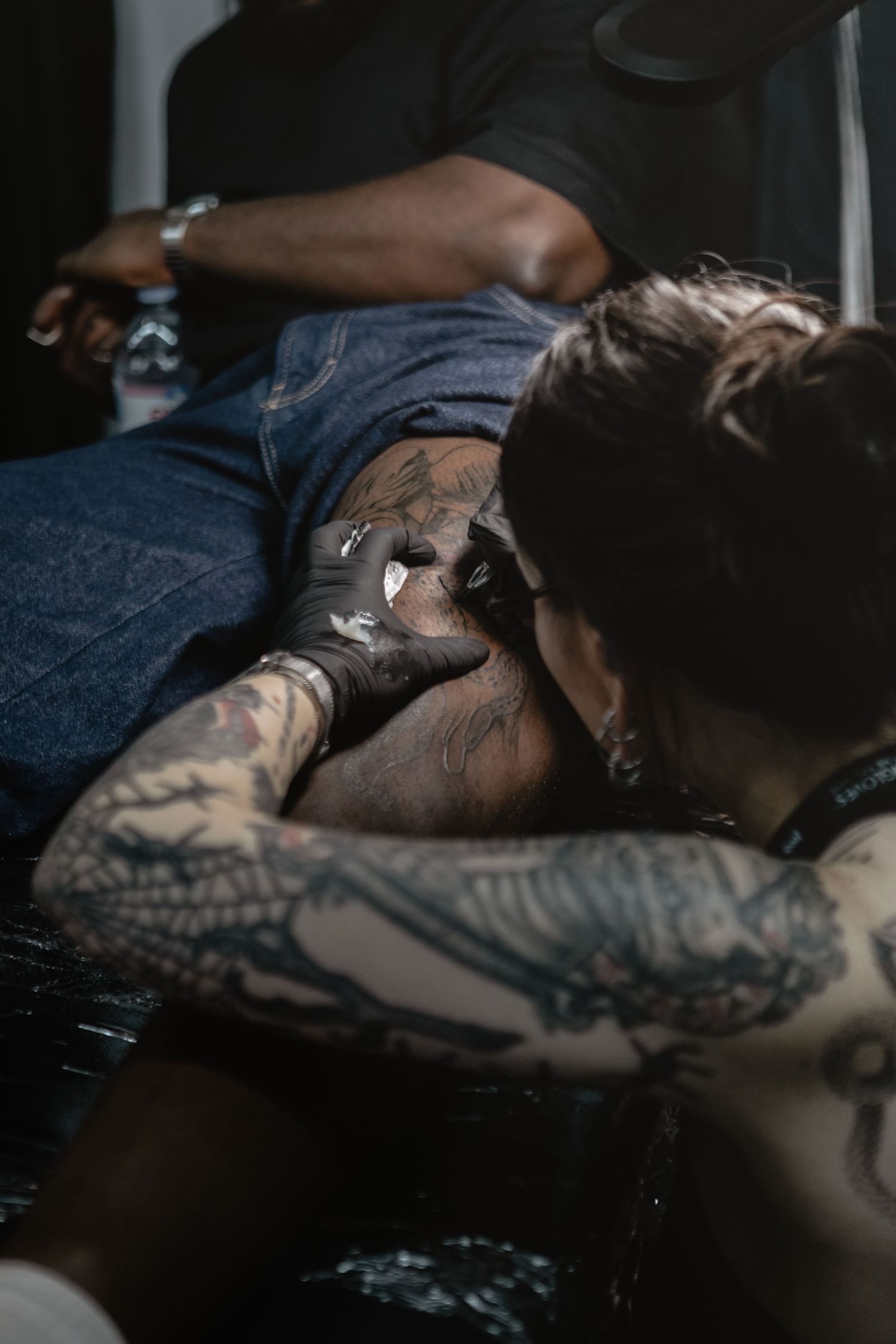 A tattoo artist wearing protective gloves works on inking a detailed design during a professional tattoo session.