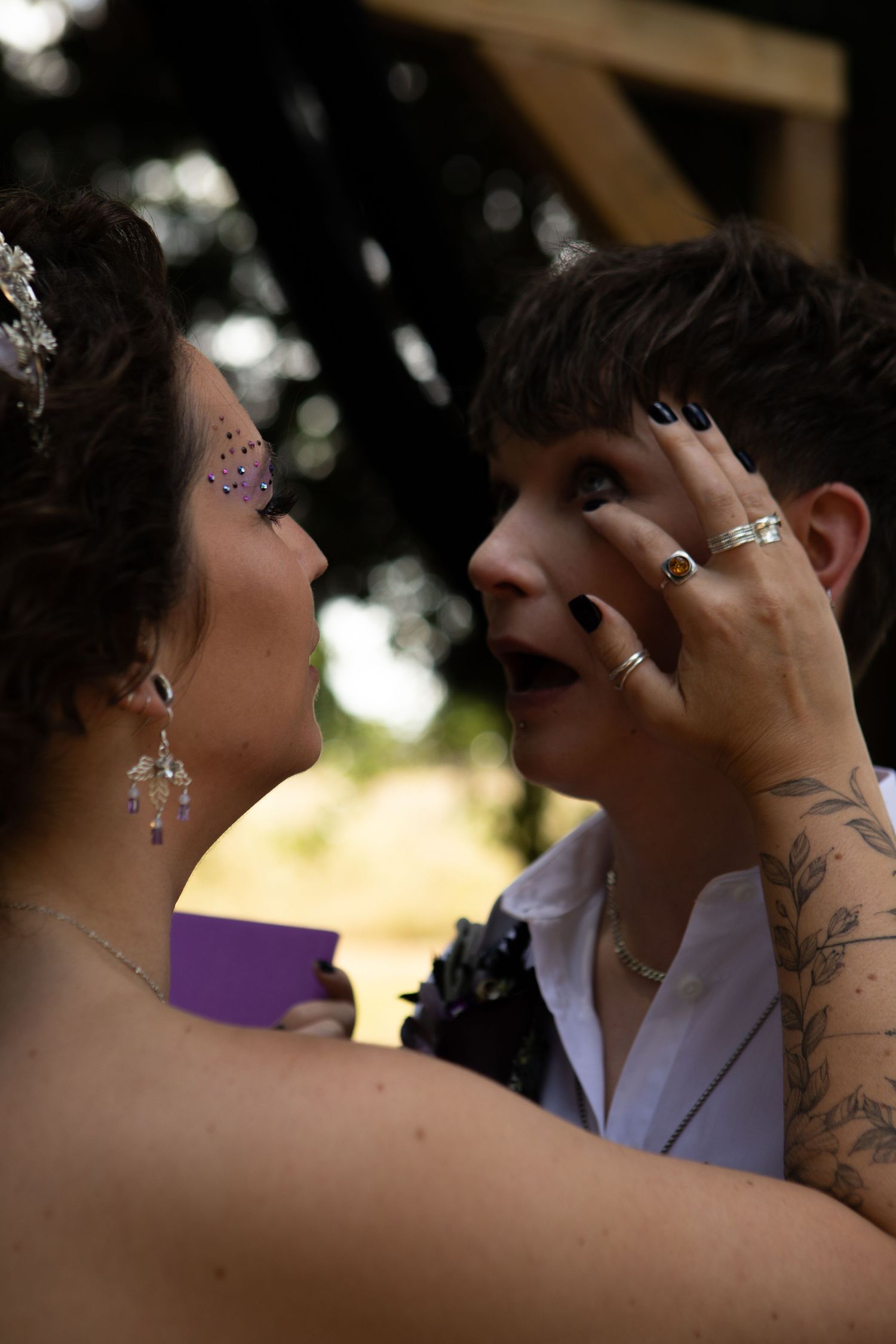 Two hands embrace in a tender moment during a romantic outdoor event with sunlit background trees visible.