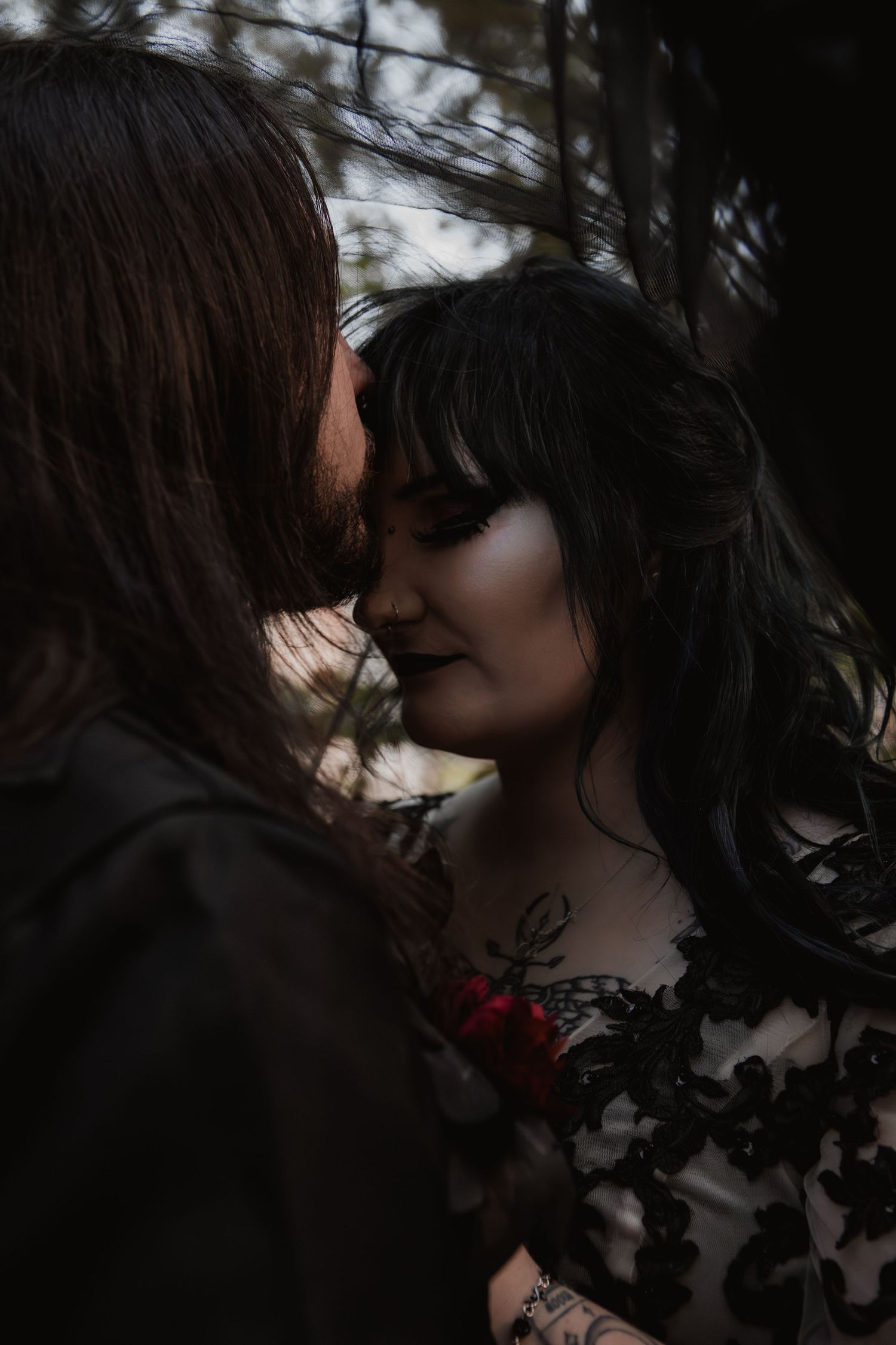 A romantic dark and moody portrait of a couple in an intimate embrace against a blurred forest background.
