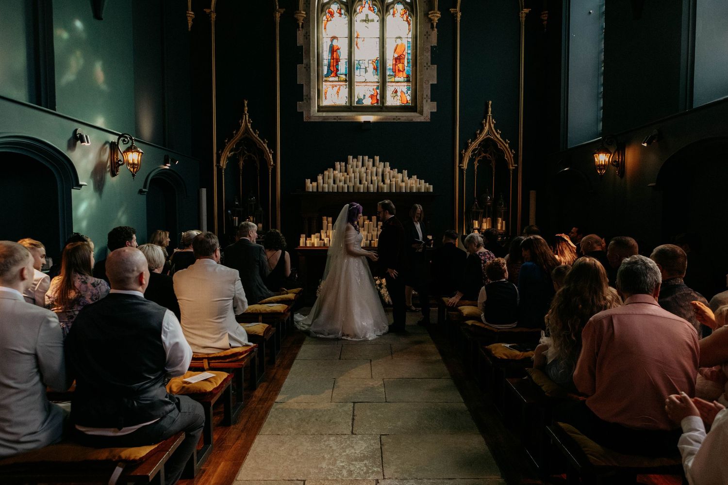 Sunlit wedding ceremony in a gothic church with guests seated along stone aisle.