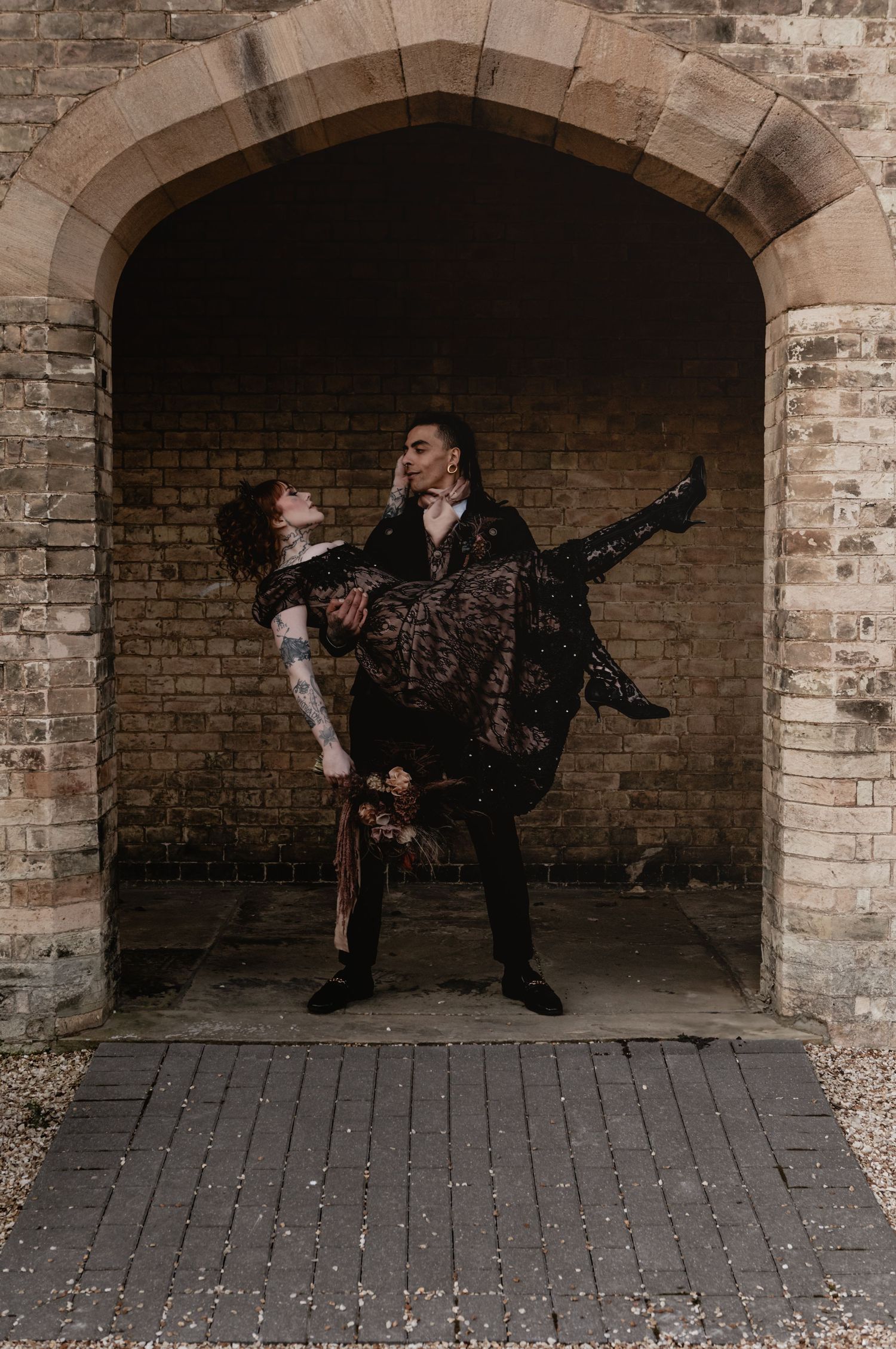 A dramatic dance pose captured under a brick archway with two performers in dark theatrical costumes.