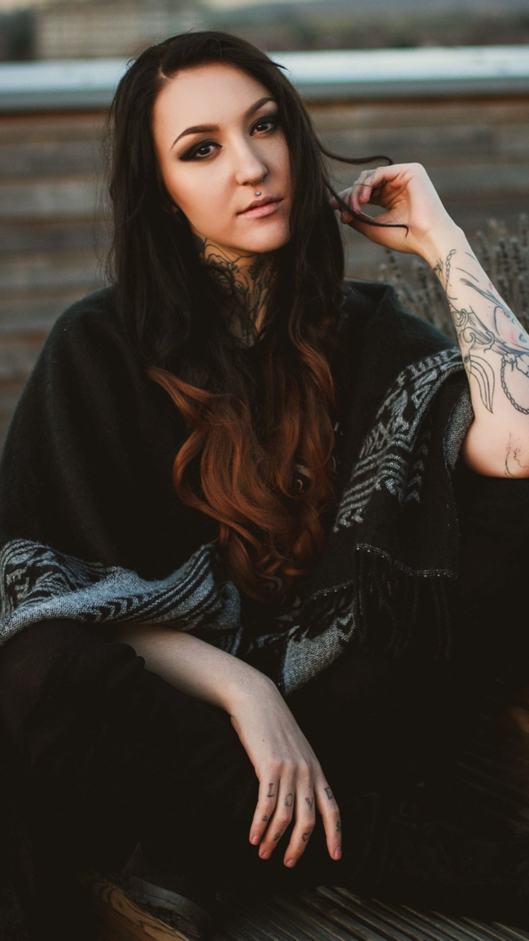 Portrait of a woman with long dark hair and tattoos wearing a black dress in moody outdoor lighting.