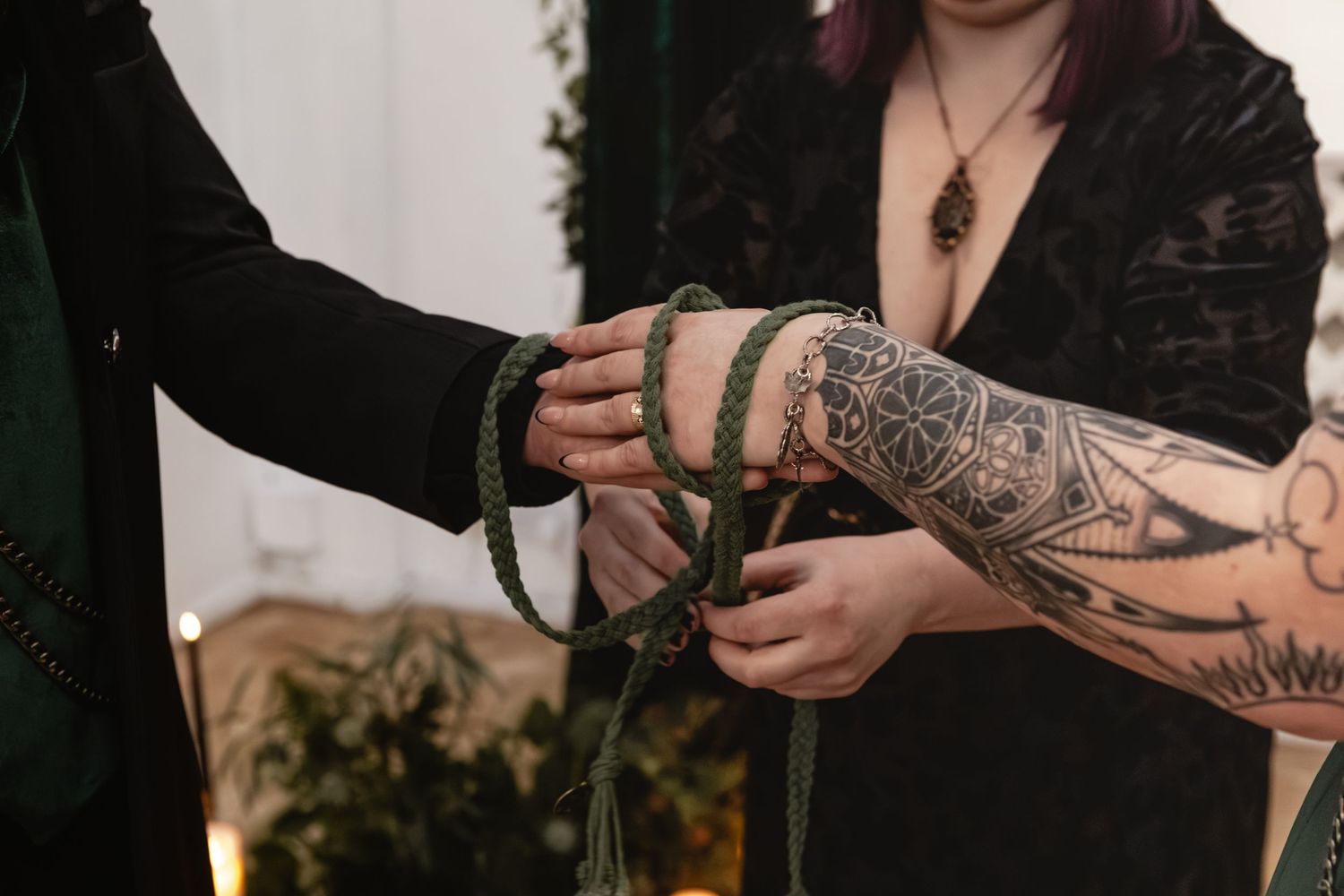 Two tattooed hands carefully arranging flowers together in a dark moody setting.
