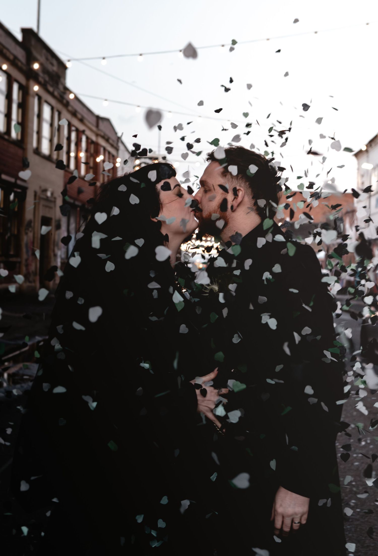 A romantic moment captured in silhouette as confetti hearts float through the air on a city street.
