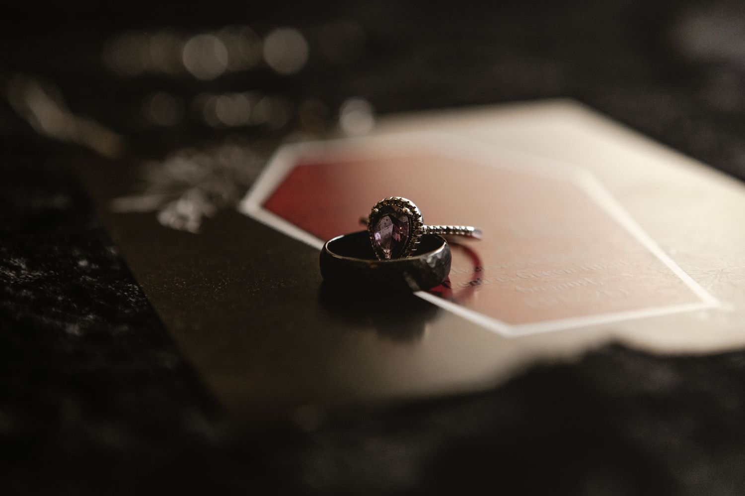Diamond engagement ring rests on top of a playing card with soft bokeh lighting in the background.
