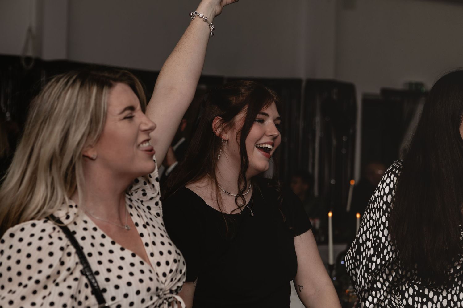 People dancing and celebrating at a lively indoor party with one wearing polka dots and another in black.