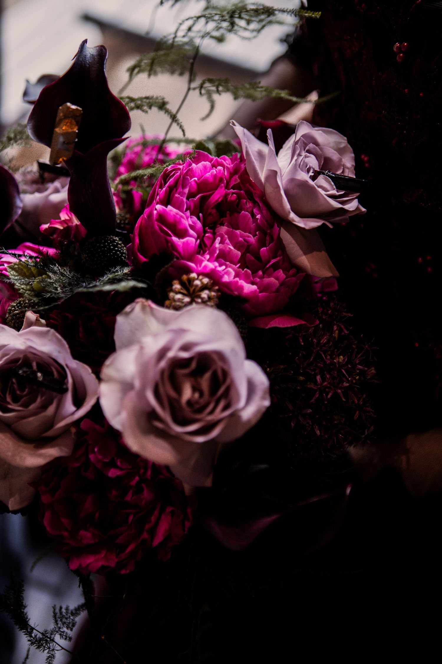 Dark and romantic bouquet with dusty pink roses and rich magenta blooms against shadowy background.
