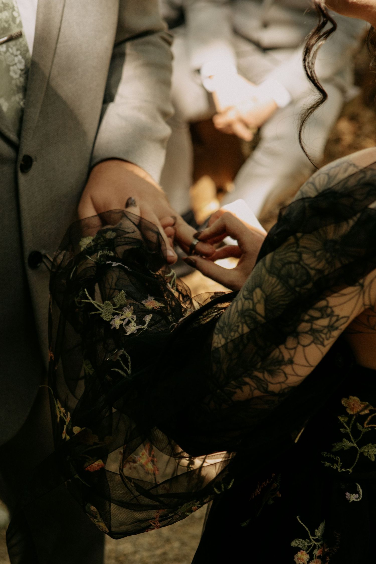 Close-up view of hands holding delicate black lace fabric with floral patterns in moody lighting.