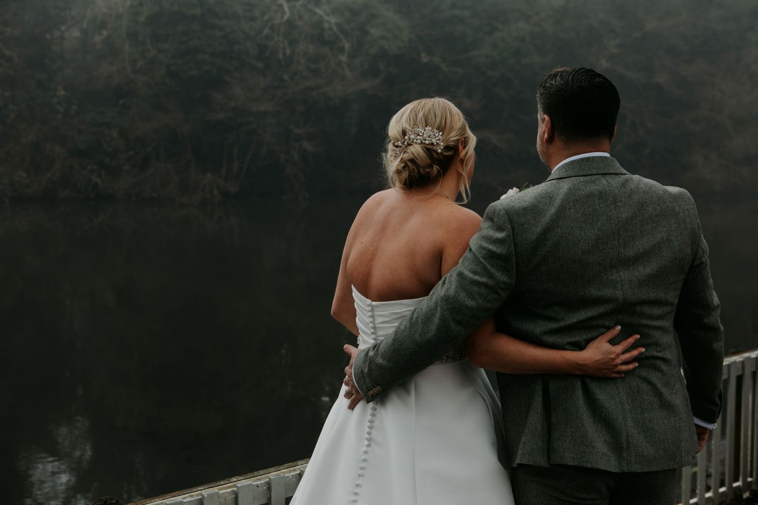 A couple embraces while looking out over a misty landscape in wedding attire.