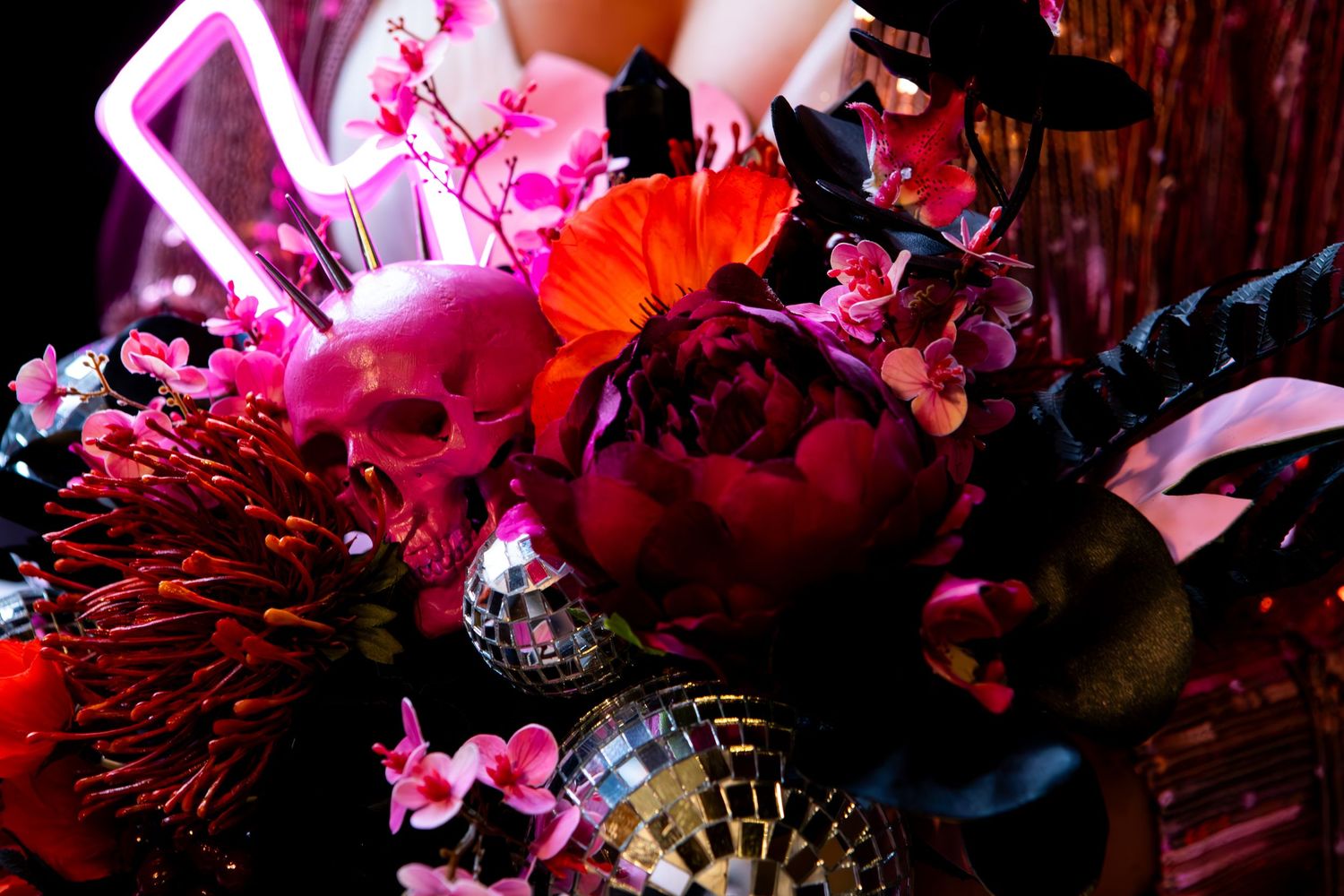 Dramatic floral arrangement with red and pink blooms illuminated by neon pink lighting and moody shadows.