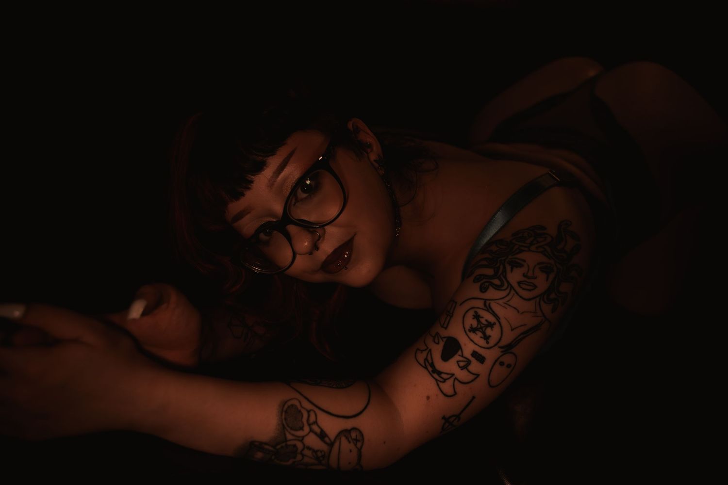Dark moody photo showing someone's tattooed arms in low dramatic lighting against a black background.