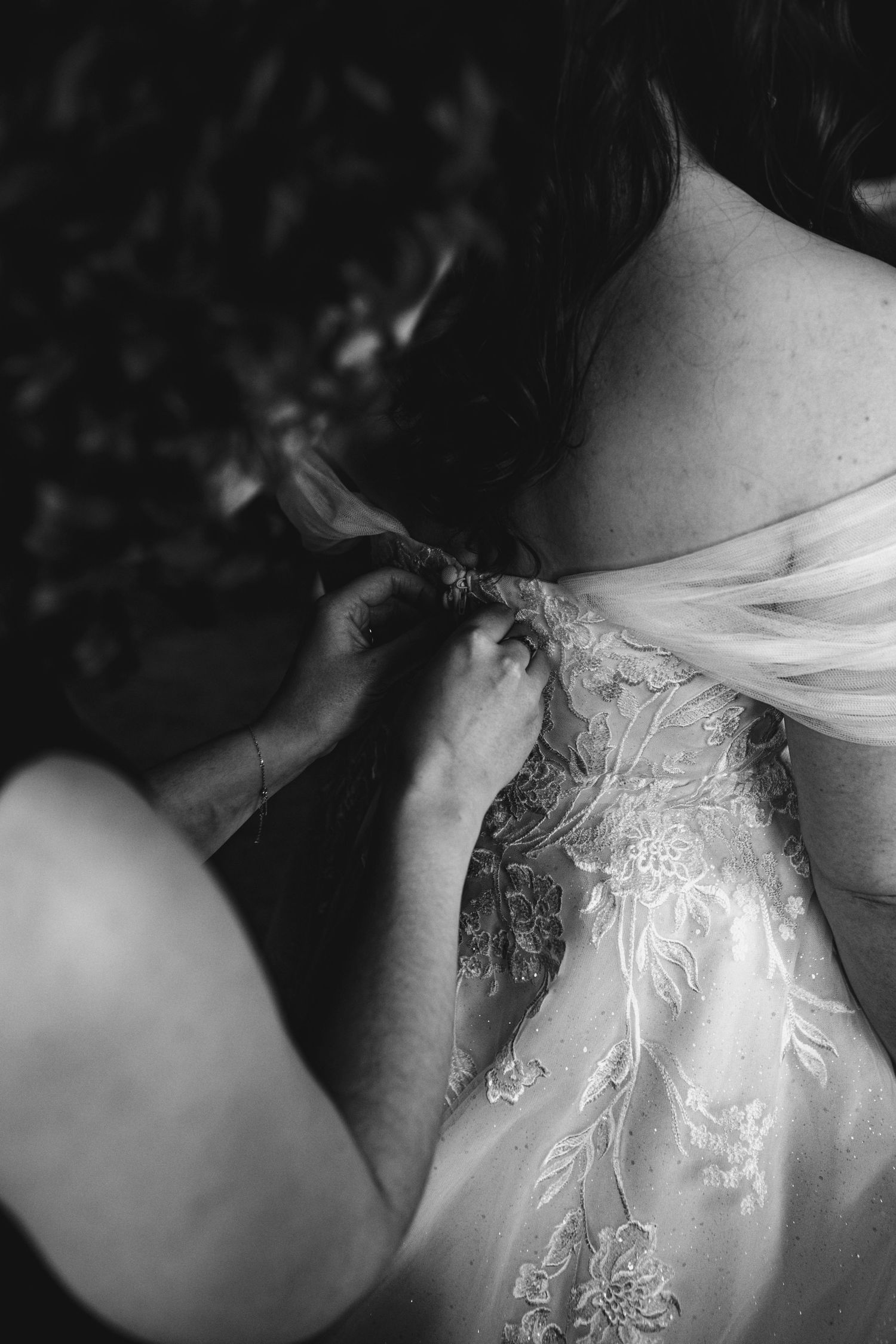 Black and white close-up of hands fastening delicate lace detail on an elegant wedding dress.