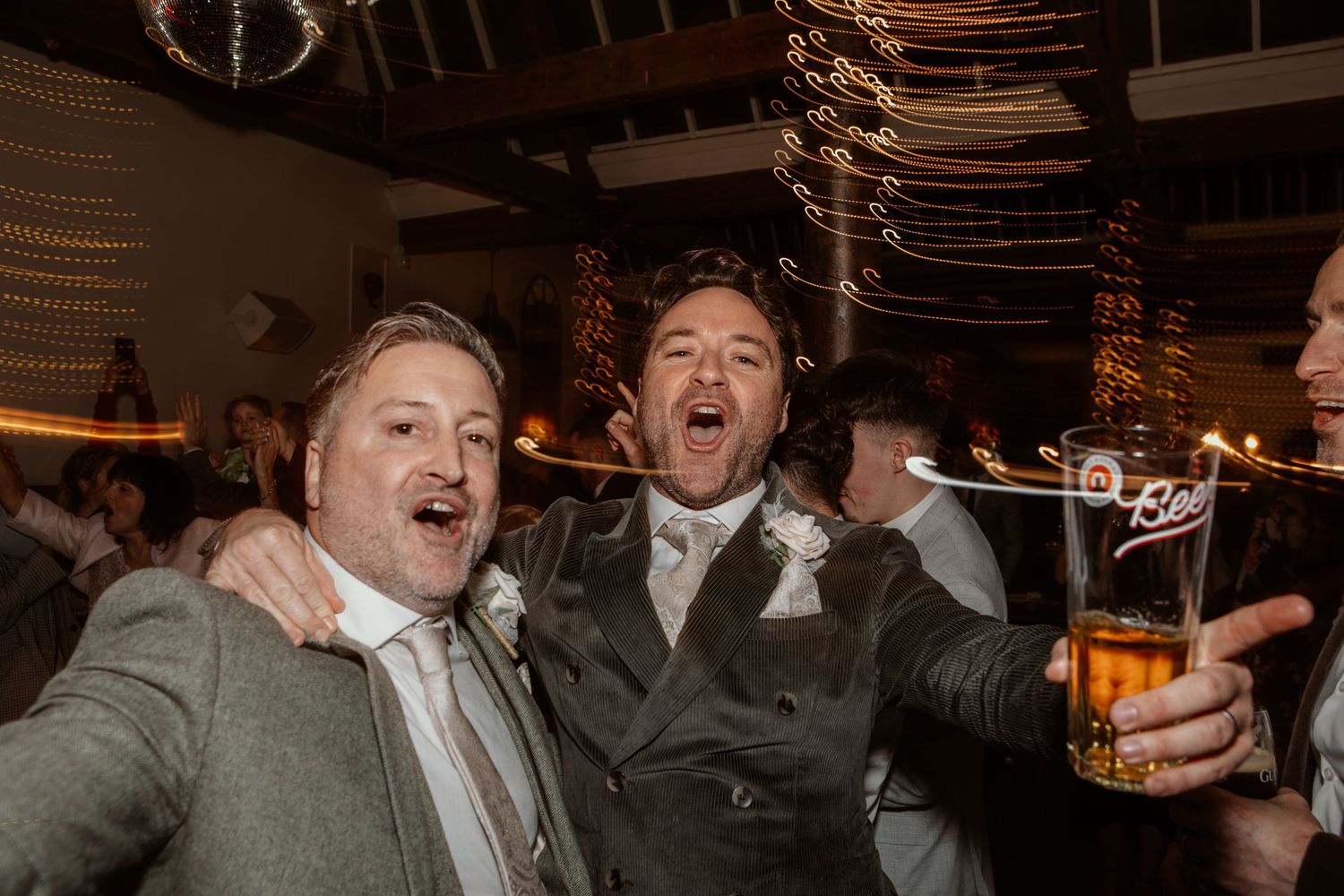 Two wedding guests sharing an exuberant celebratory moment at a reception with string lights.