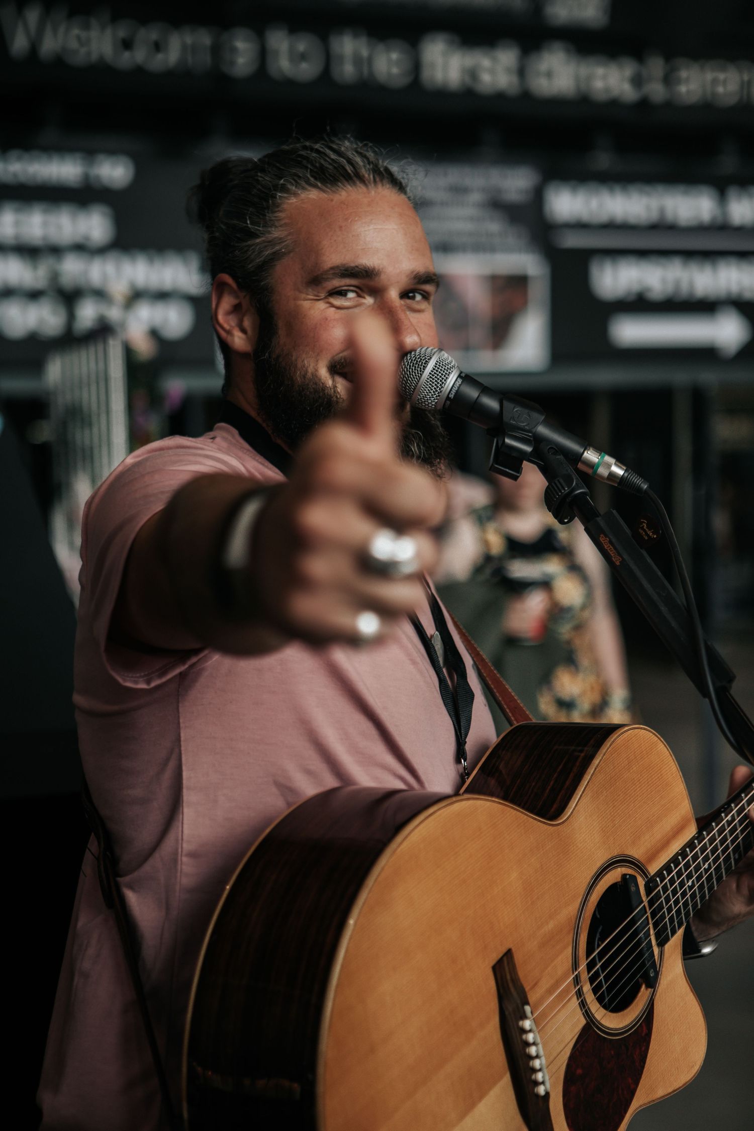 A musician performs on stage with an acoustic guitar while holding a microphone at a live music venue.