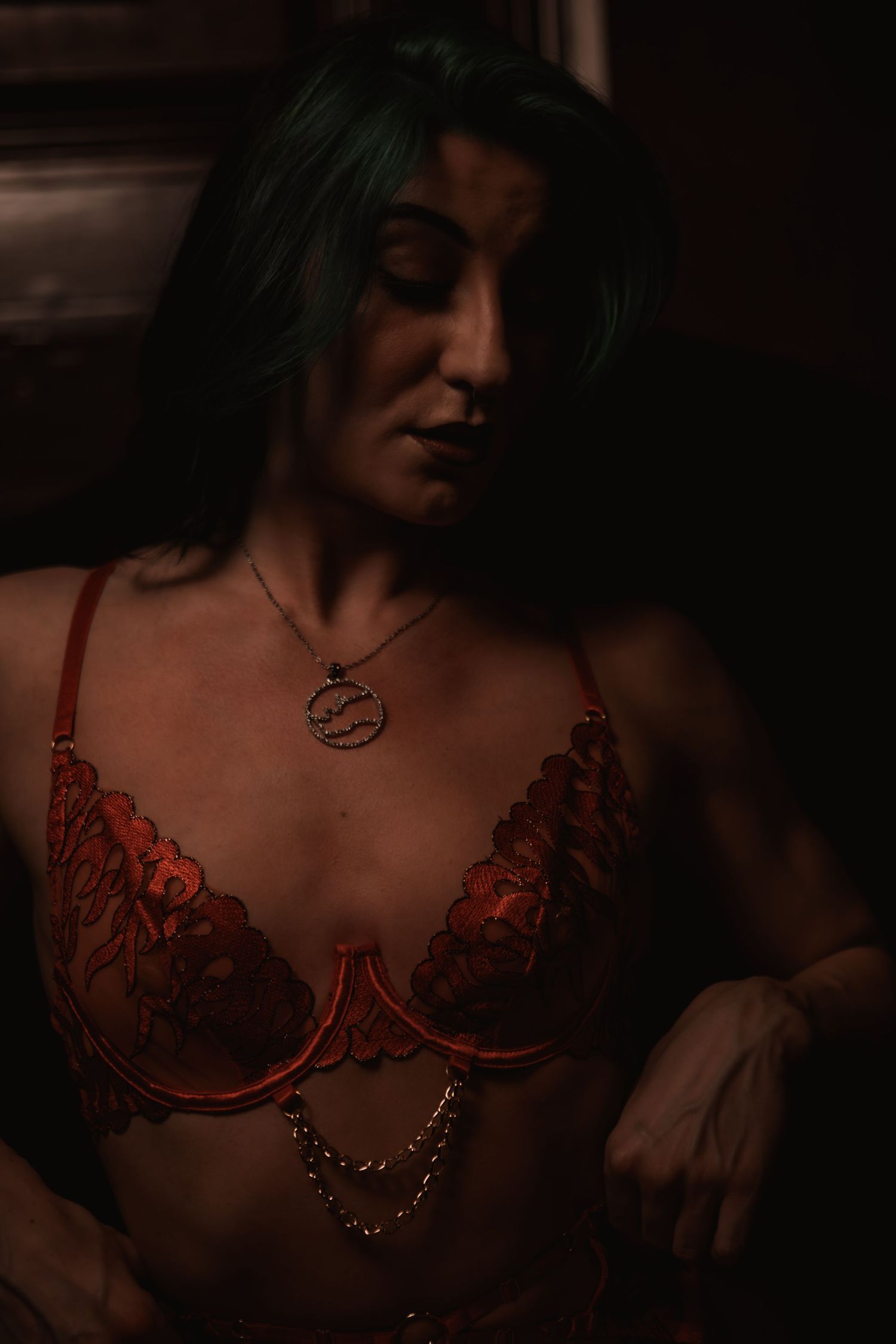 Artistic moody boudoir photo showing dark silhouette wearing red lace lingerie and pendant necklace in dim lighting.