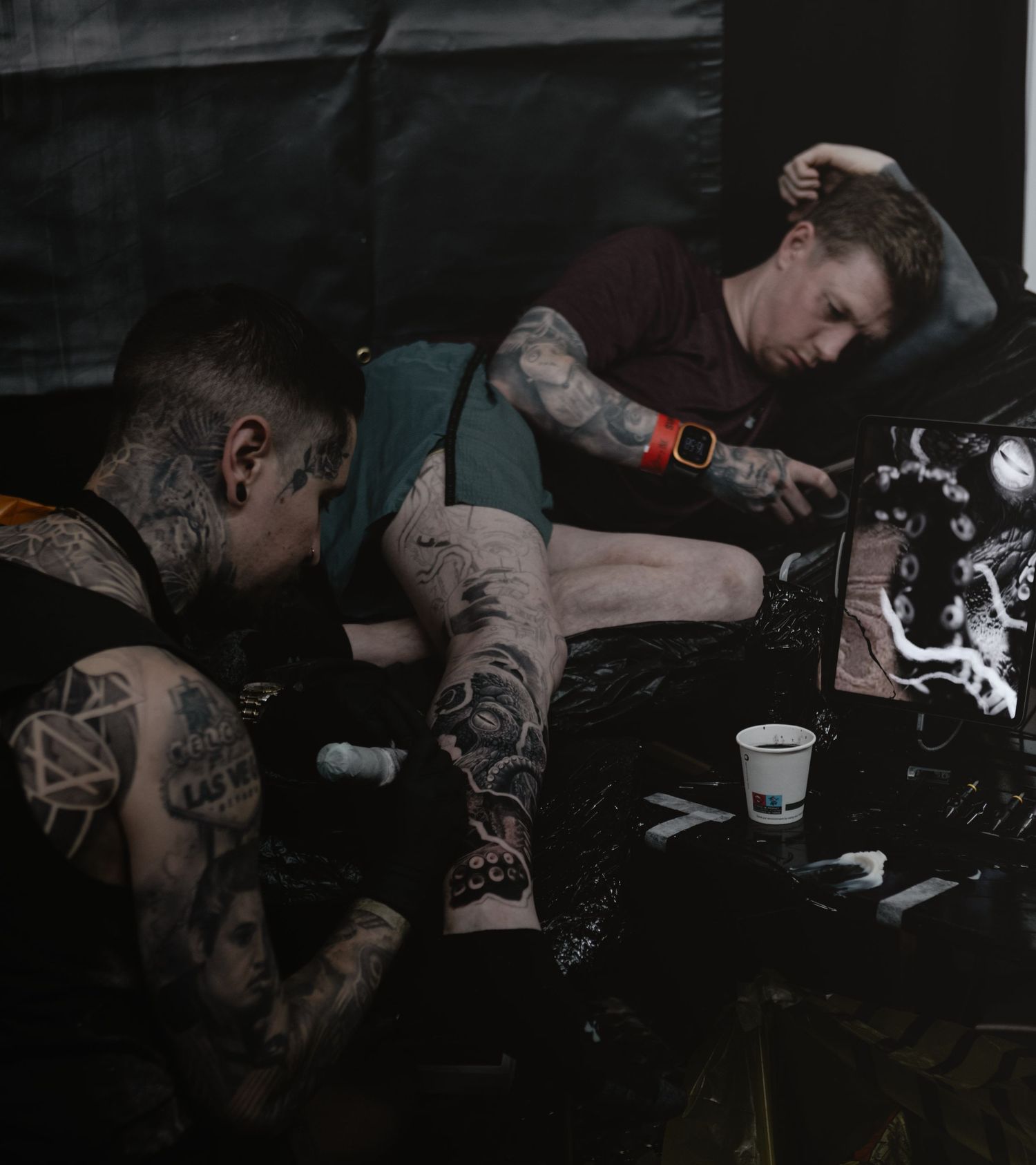 Tattoo artists working in a dimly lit studio, showing detailed arm tattoos and professional equipment.