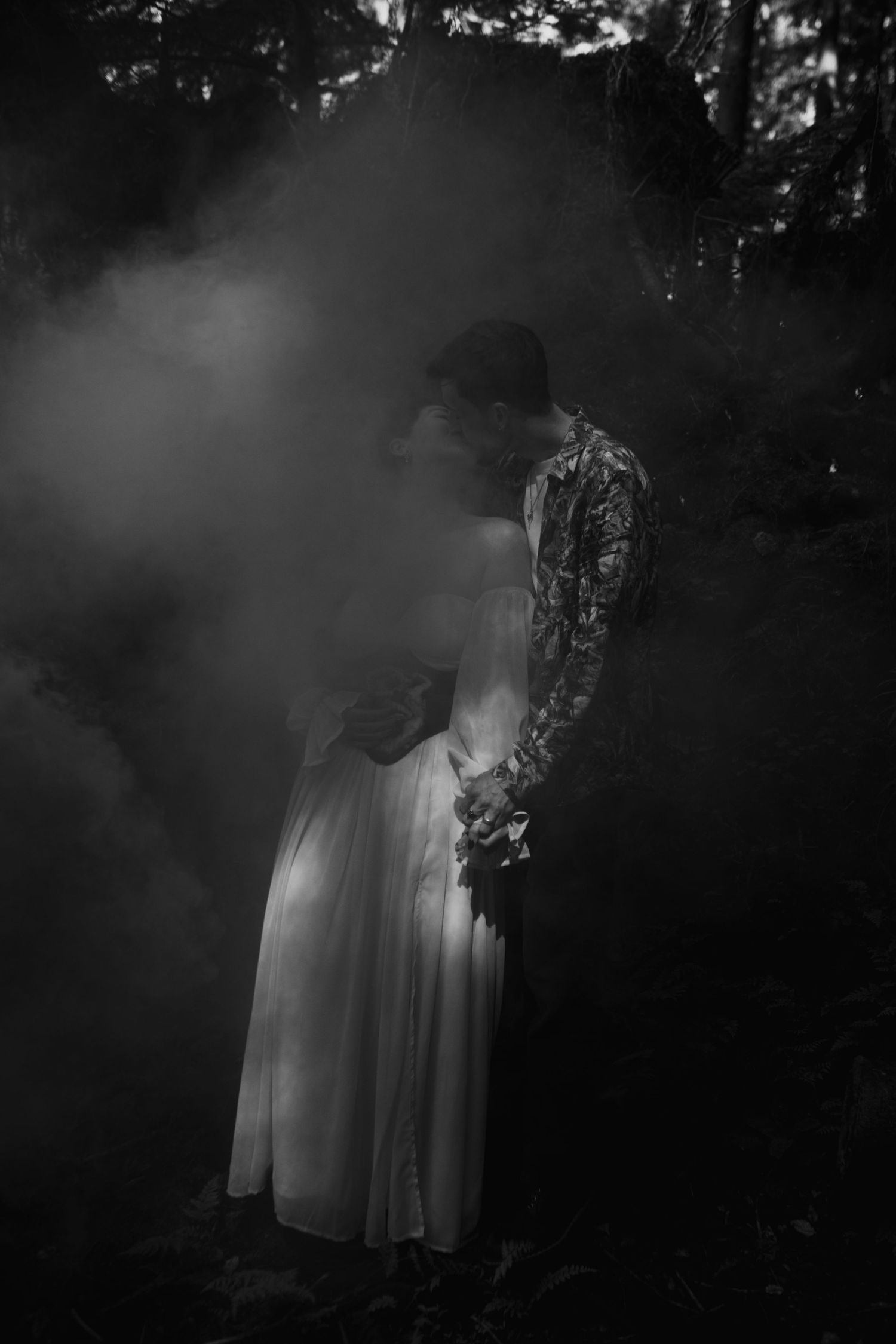 An artistic black and white photograph with fog showing a white dress and floral pattern in a misty forest setting.
