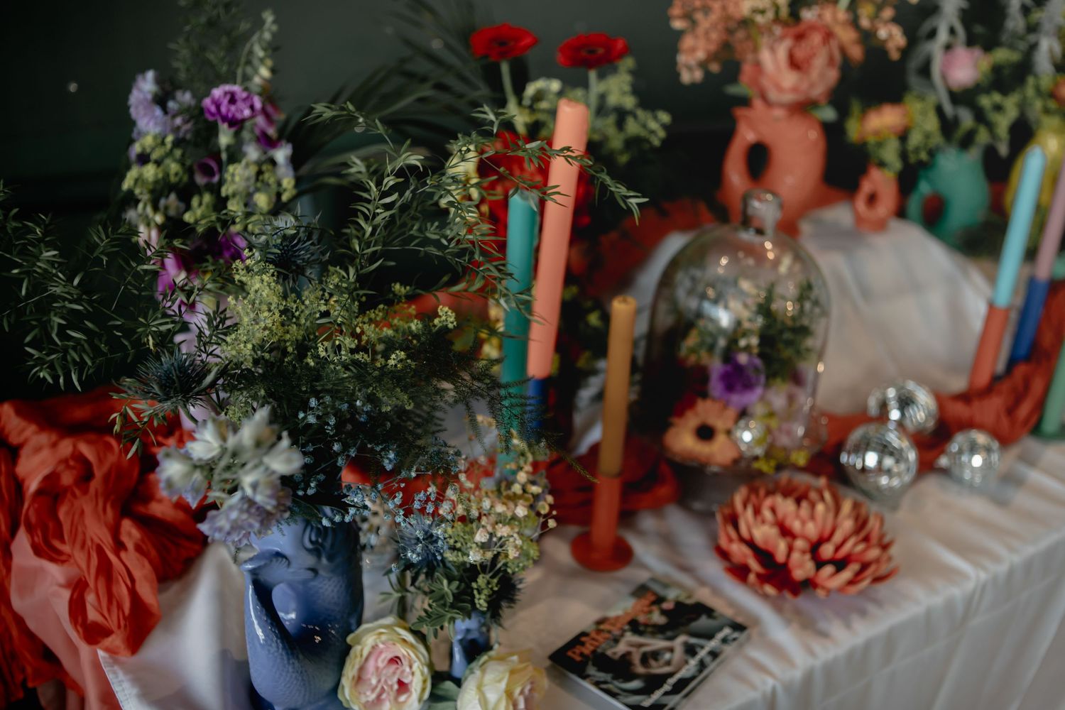 Colorful floral table decor featuring eclectic candlesticks, dried flowers and small decorative skulls in a moody setting.