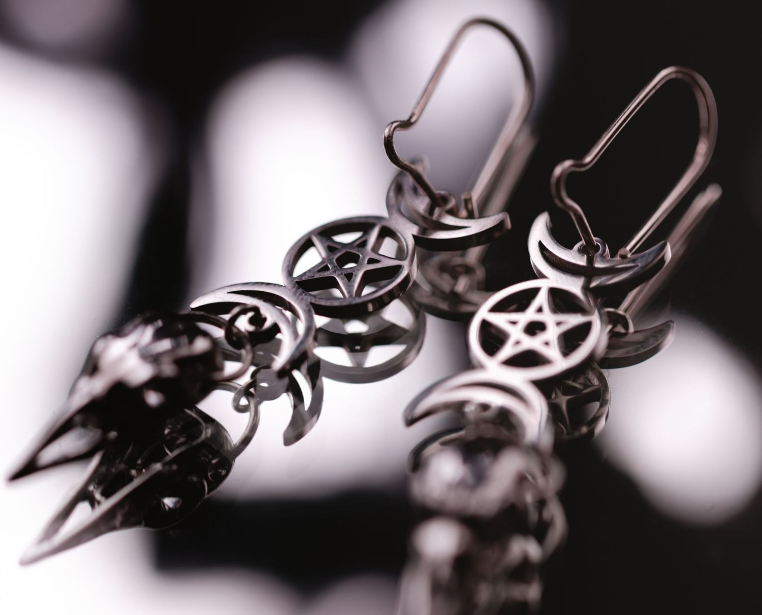 Dangling silver pentagram charm earrings with gothic spikes on a blurred background.