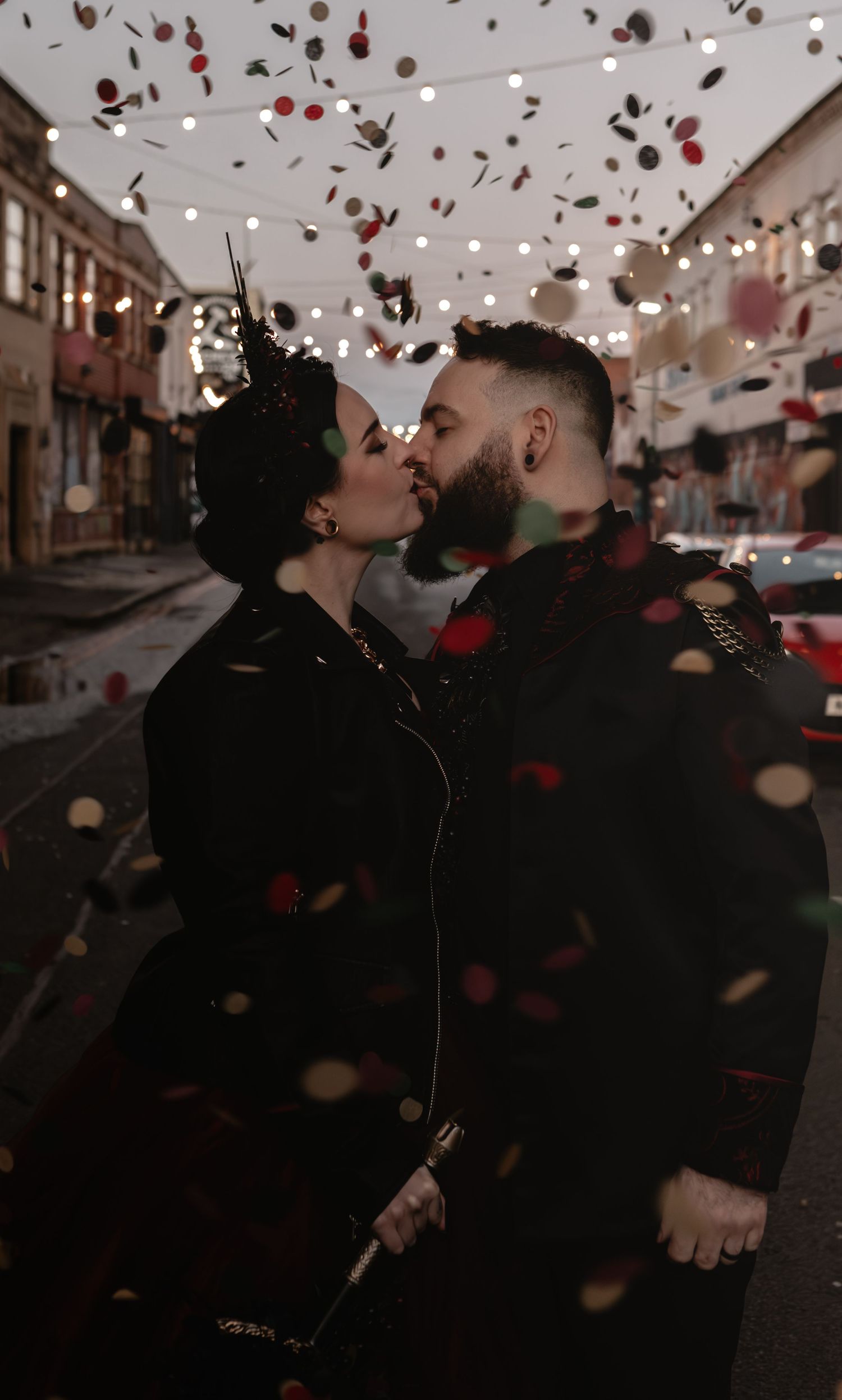 A couple kisses on a street while rose petals fall around them.