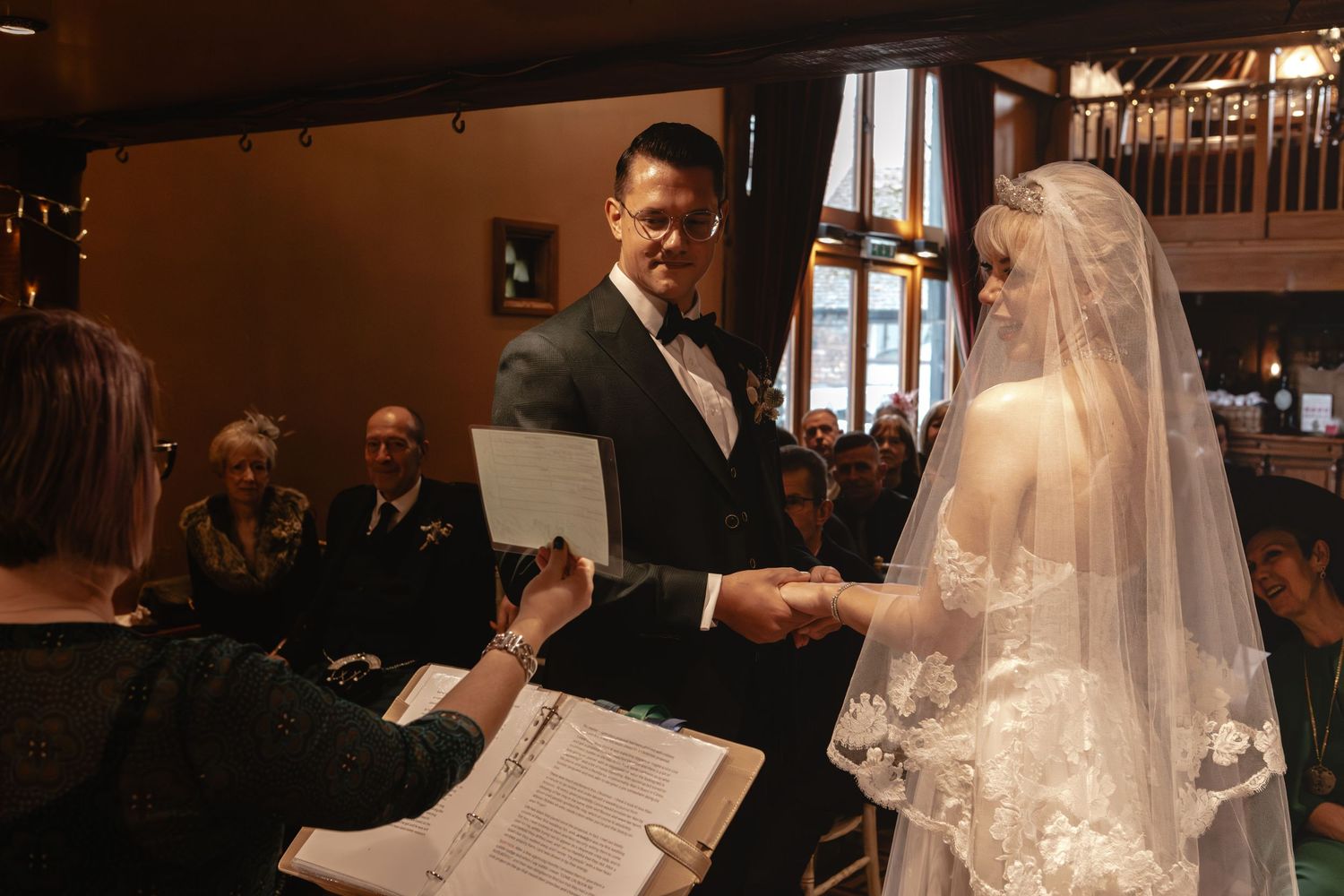 A wedding ceremony taking place in a rustic indoor venue with guests seated in rows.