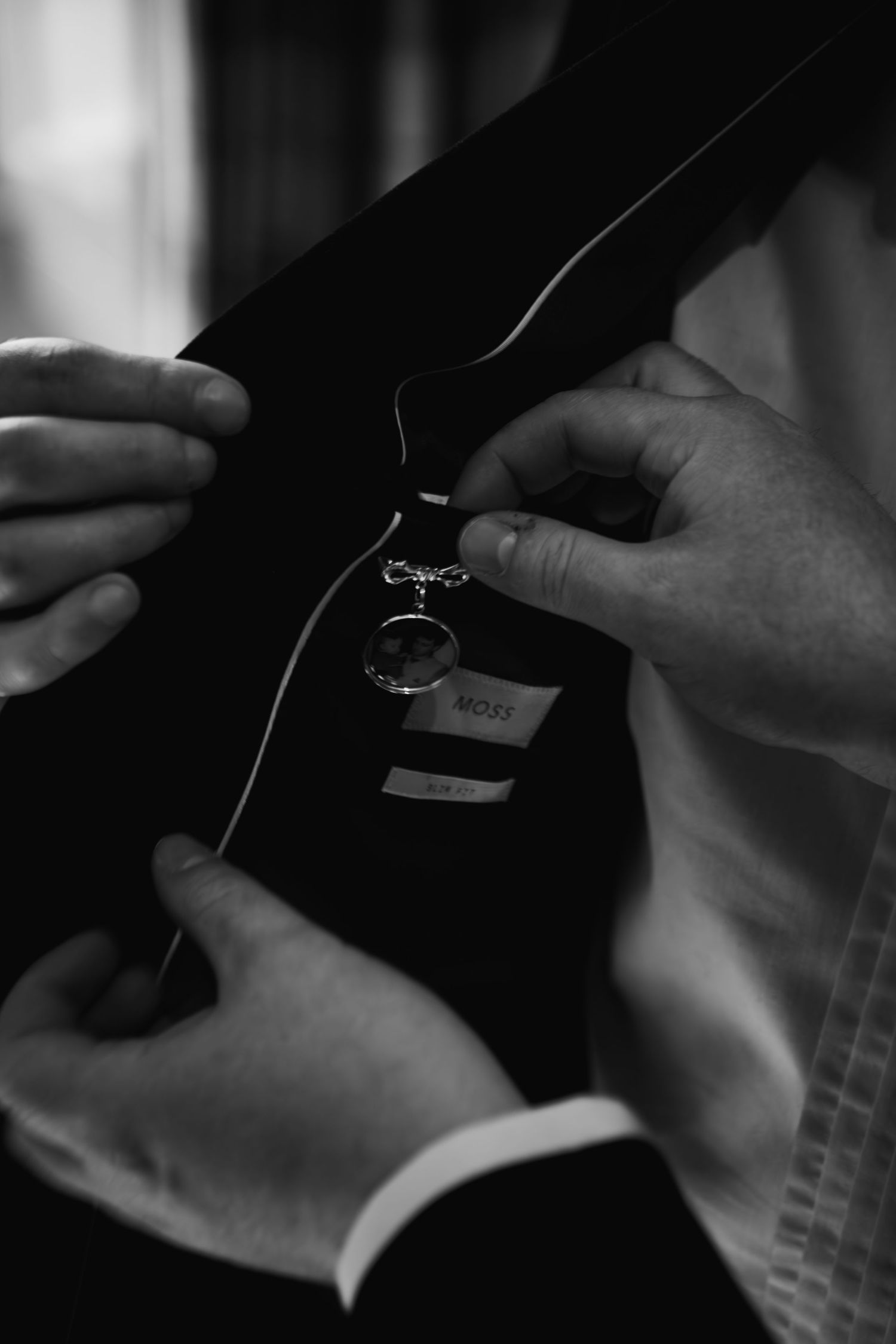 Close-up black and white shot of hands adjusting a ring on a formal suit jacket lapel.