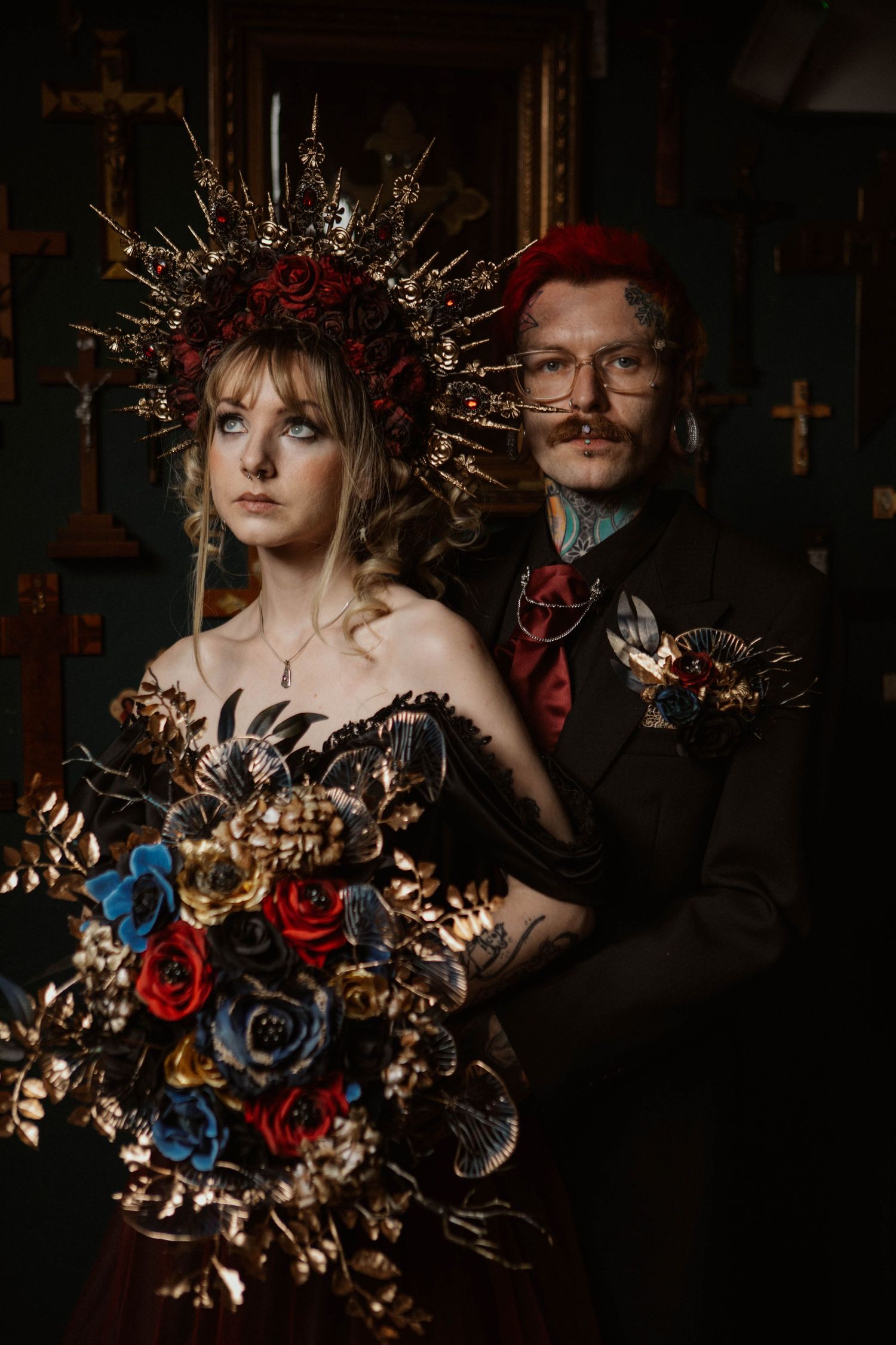 Gothic wedding couple in dark setting with ornate crown and colorful floral bouquet.